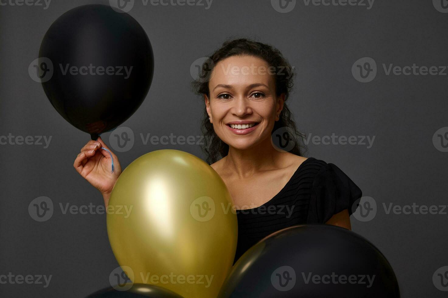 Close-up face portrait of African woman with beautiful smile posing with black and gold air balloons against gray background with copy space. Concept of Black Friday and gold credit card for shopping photo