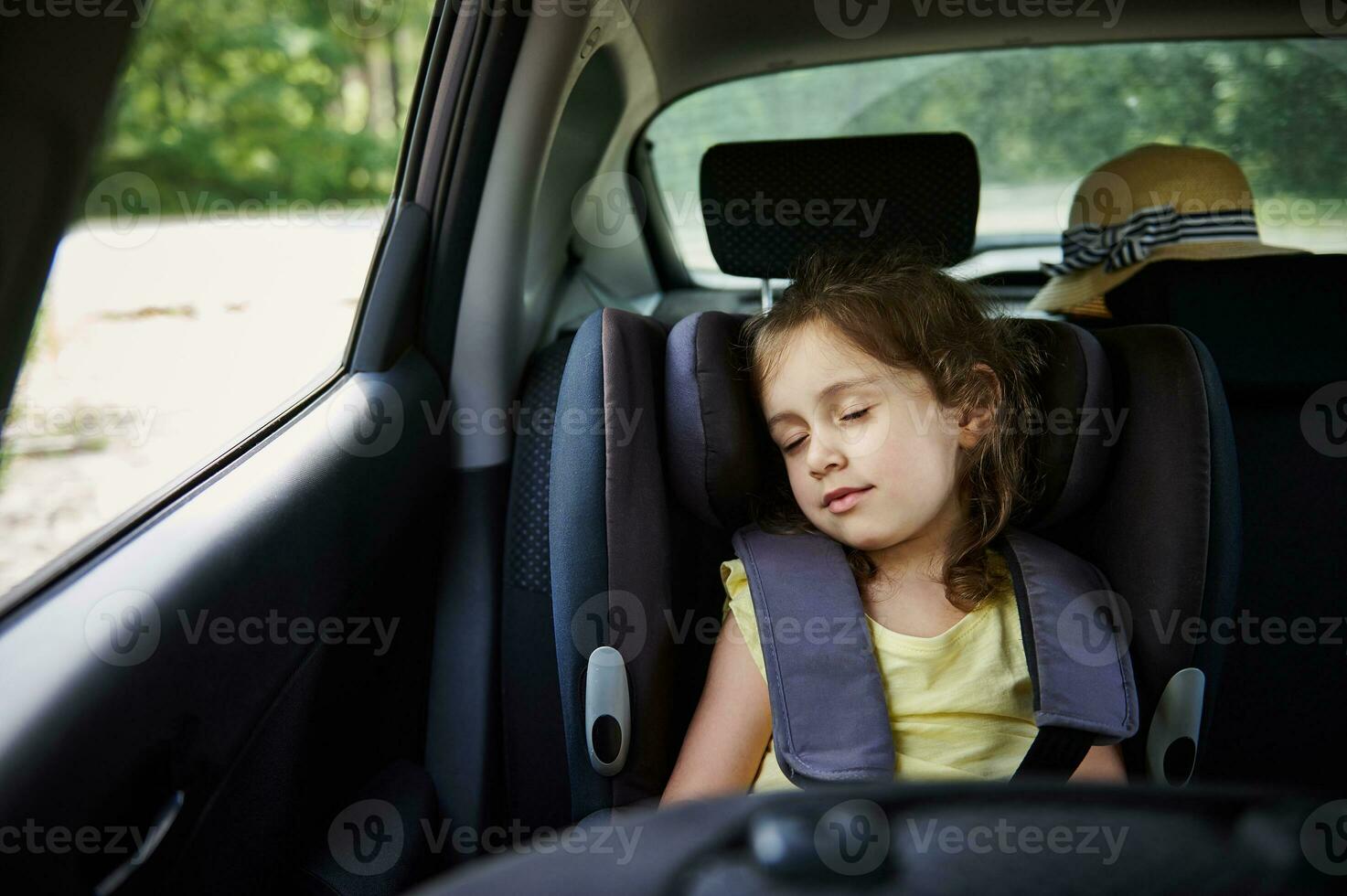 Safe movement of children in the car. Little girl sleeps in a booster seat in the car. Child safety seat. photo