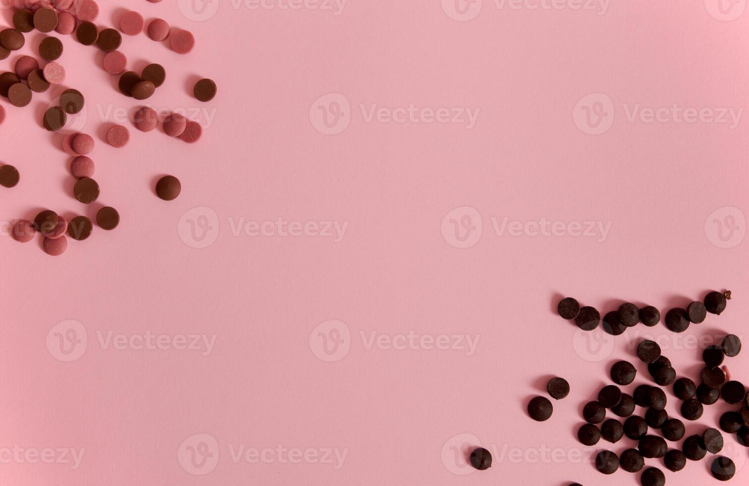 Flat lay composition with scattered pink and dark chocolate pills in corners of pink background with copy space photo