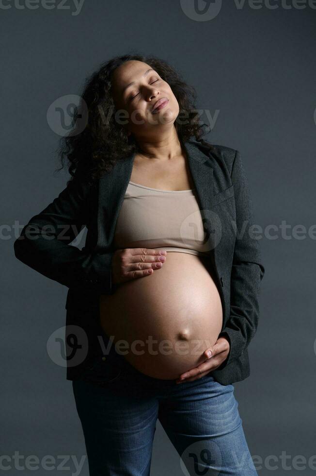 Gravid woman, expectant mother strokes her pregnant belly over gray background. 40 week of happy carefree pregnancy. photo