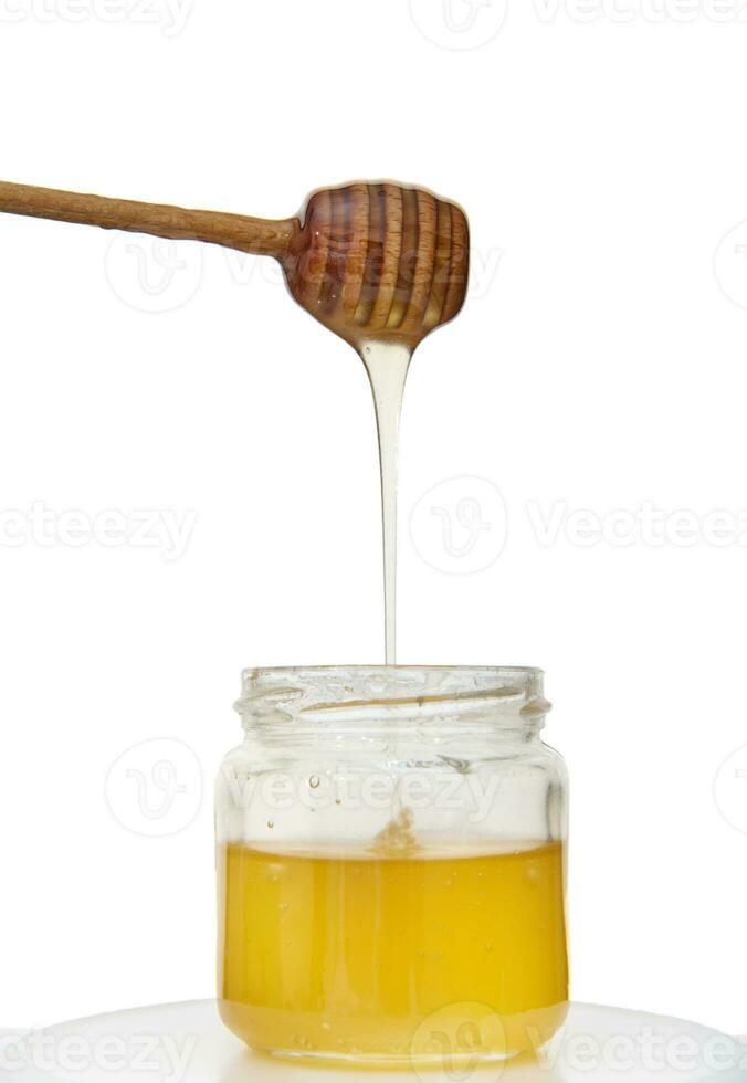 Dripping honey from honey dipper into jar of organic healthy sweet natural honey, isolated over white background with copy space photo