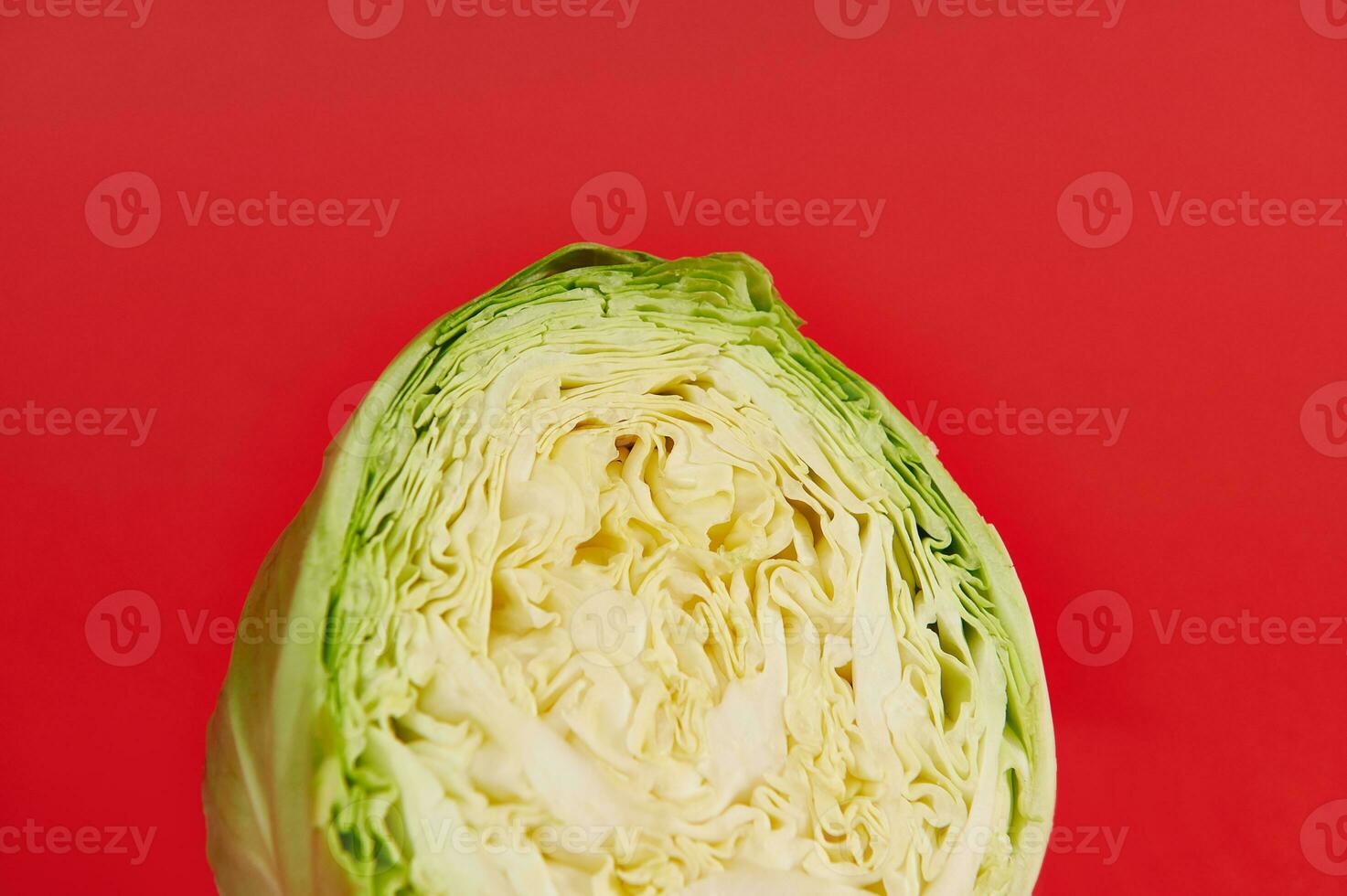 Cropped image of a half cut young green cabbage on a red background with copy space. Color contrast. photo