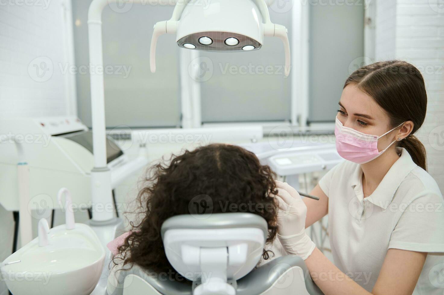 joven hembra dentista higienista vistiendo protector médico máscara examinando odontología clínica pacientes boca utilizando inoxidable acero estéril dental herramientas. mujer consiguiendo su diente reparado a del dentista oficina foto