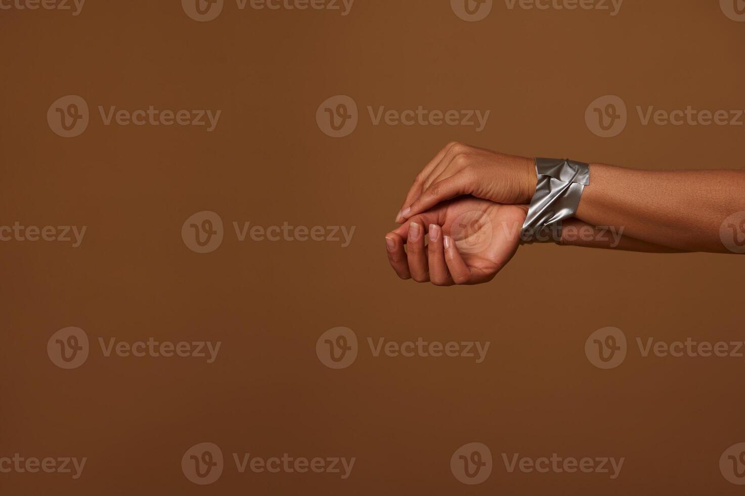 Cropped view of female hands tied with duct tape against a dark beige background. Social concept for International Day to End Aggression, Inequality and eliminating violence against Women. Copy space photo