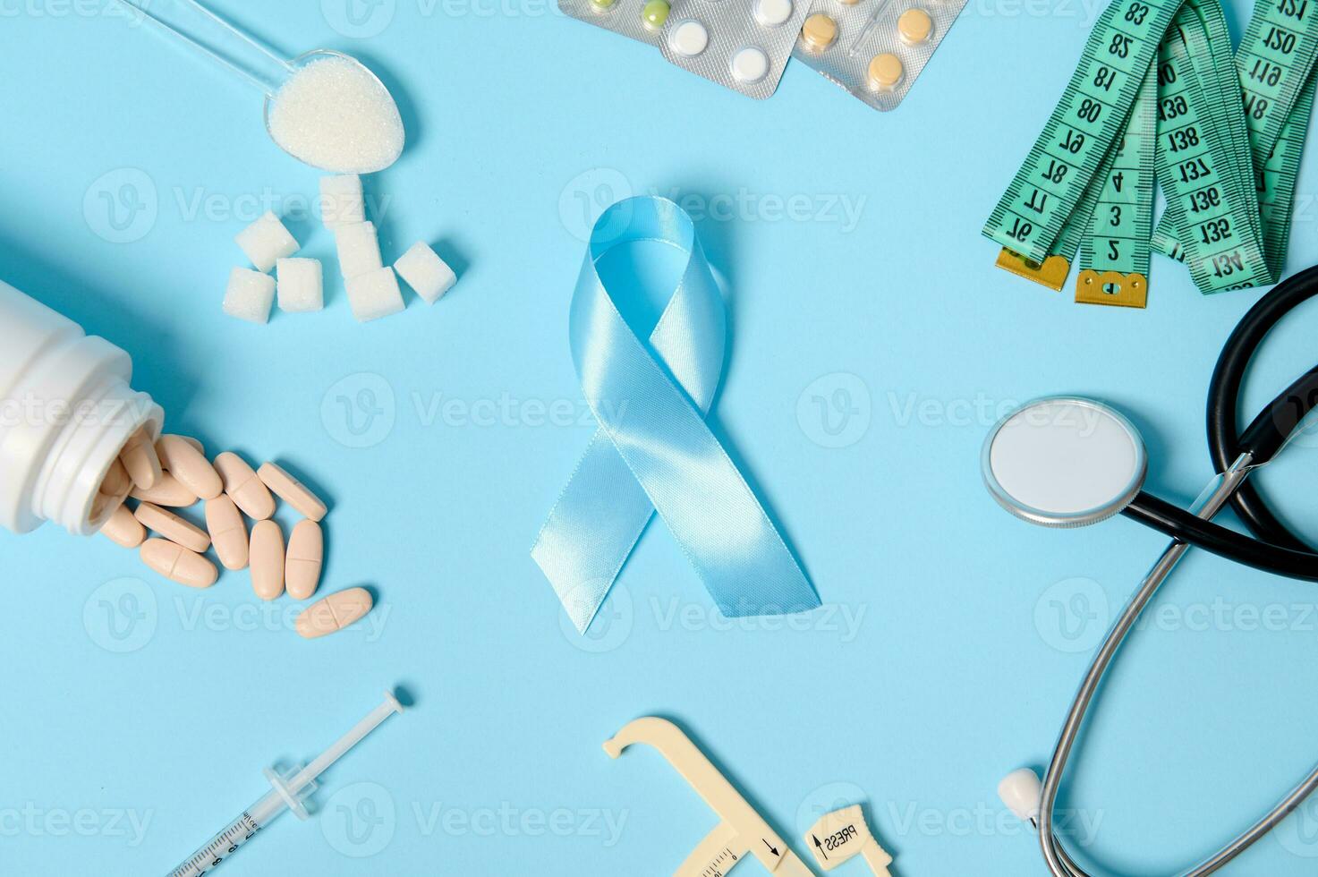 Blue Diabetes Awareness ribbon at colored background center with scattered pharmaceutical pills, blisters of tablets, insulin syringe, stethoscope, caliper , measuring tape and refined white sugar photo