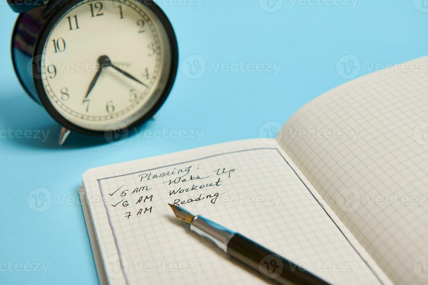 Cropped image of an open organizer with plans for the day, ink pen and alarm clock on blue background with copy space photo