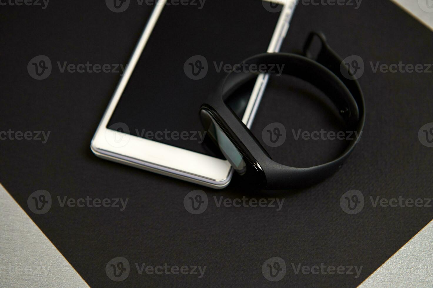 Mobile phone and digital watch or black fitness tracker on a black sheet of paper on a gray background. Black and white still life. Flat lay photo