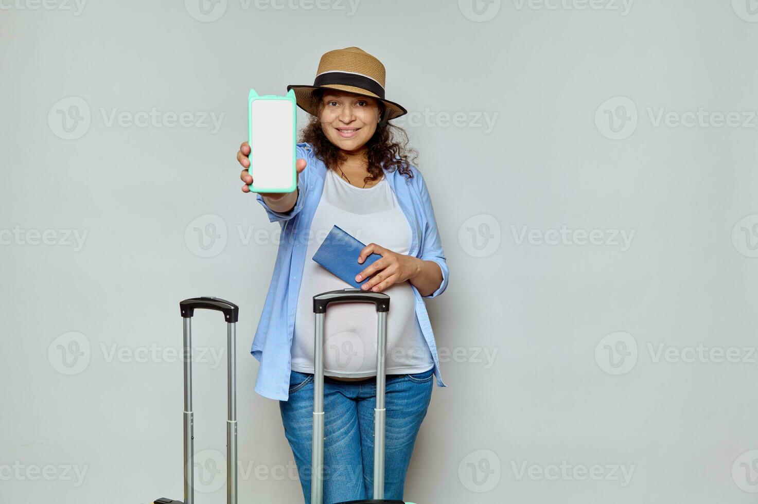 encantador embarazada mujer turista pasajero participación fuera a cámara un moderno teléfono inteligente con blanco blanco Bosquejo digital pantalla foto