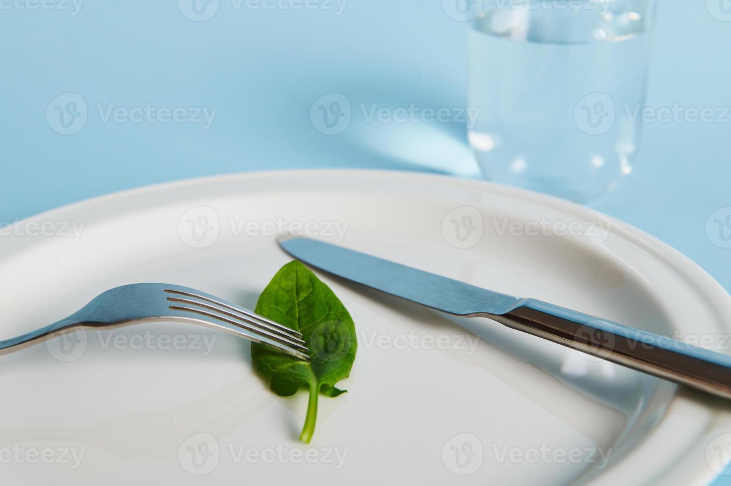 Closeup of a spinach leaf on a plate, fork, knife and glass with water on blue background. photo