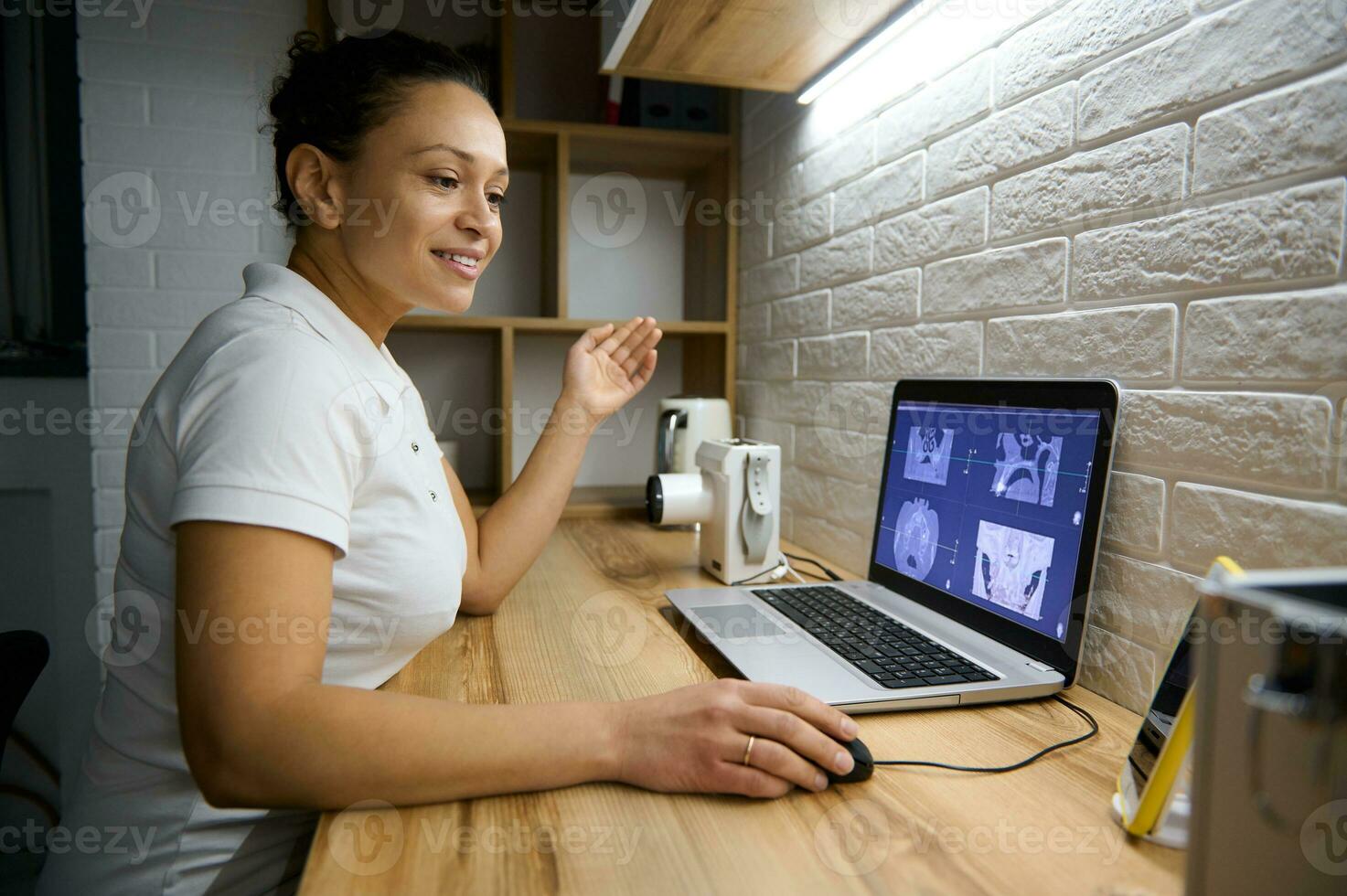 Female doctor dentist sitting in front of a laptop with a panoramic x-ray of the human teeth and consulting a patient on a video call about the treatment. Online consultation concept in medical sphere photo
