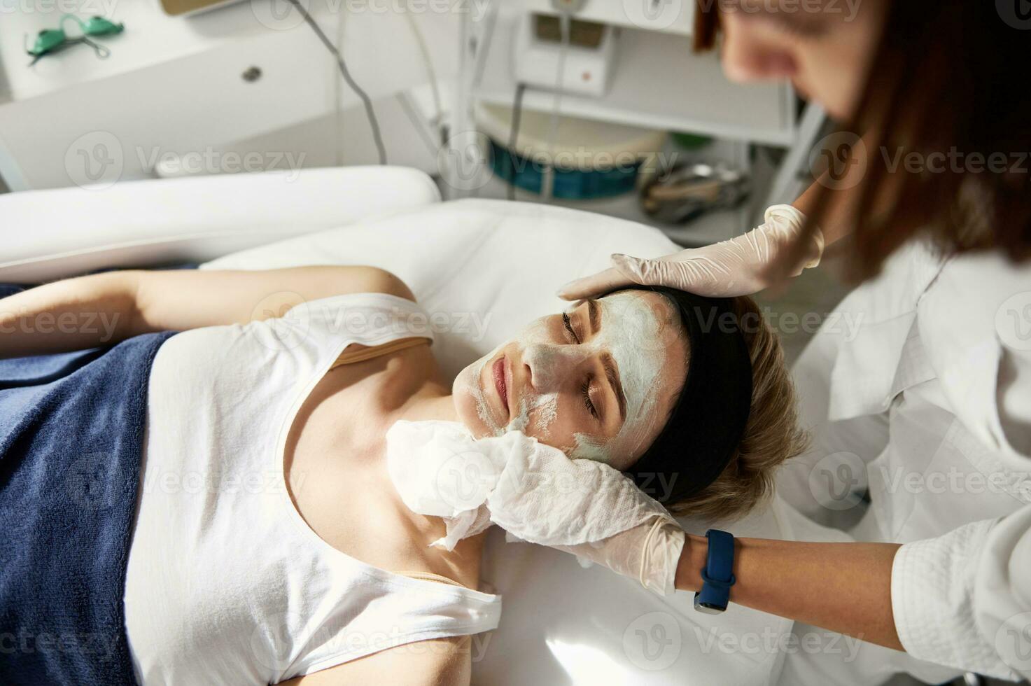 High angle view of beauticianperforming beauty procedure on woman face, removing the rest of cosmetic product using special wet serviettes. Professional skin care in cosmetology clinic photo