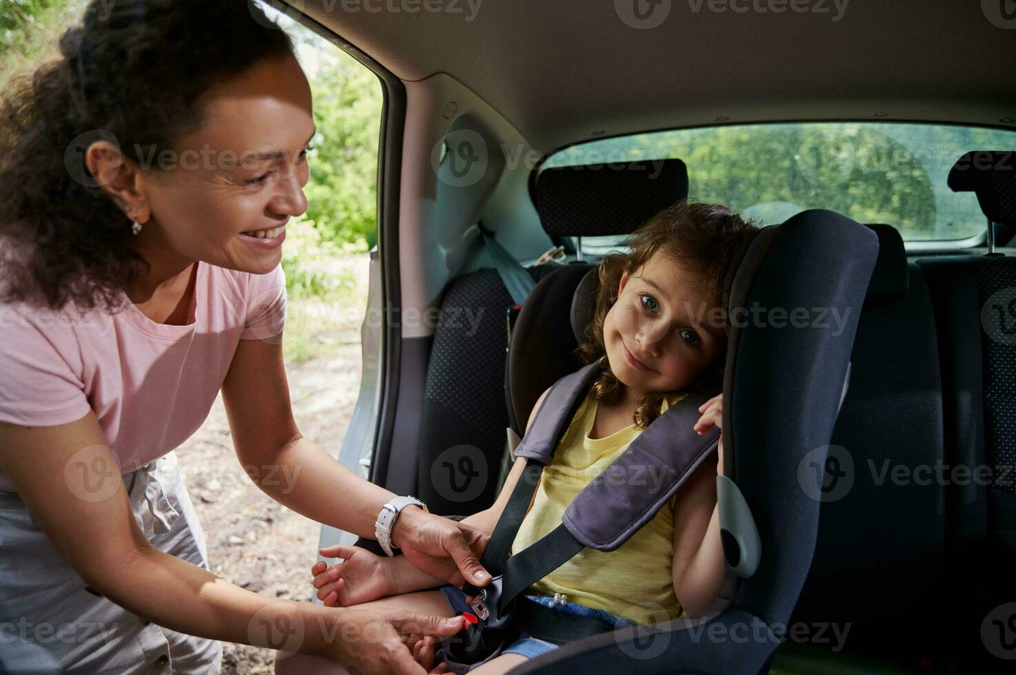 Woman puts her daughter in the child car seat and fastens the child with a seat belt. Safety of traveling in a car with children photo