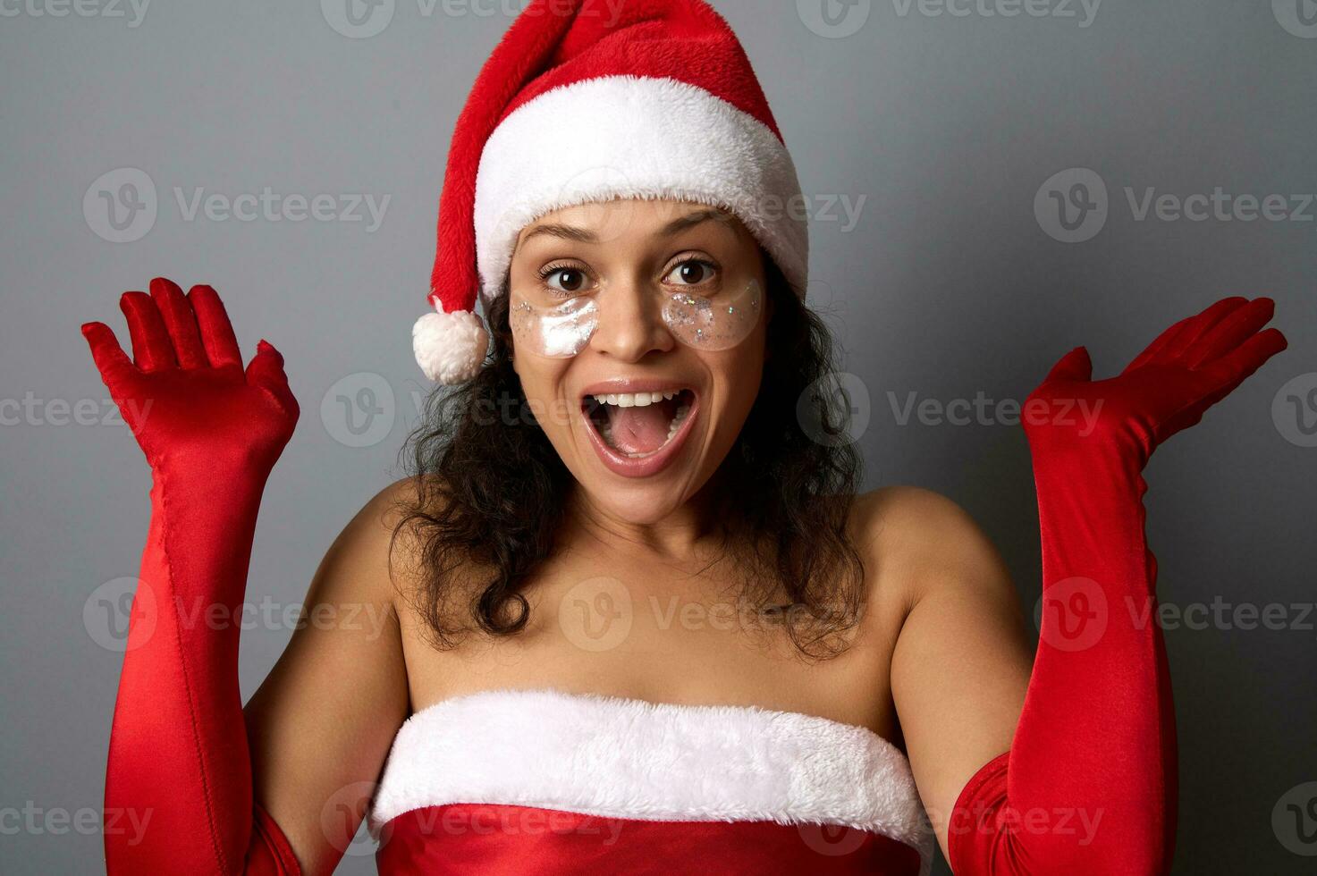 contento hermosa mujer con brillante suavizado ojo parches debajo ojos , vestido en Papa Noel atuendo pone su manos palmas arriba y se regocija mirando a cámara. alegre Navidad, nuevo año y cosmetología concepto foto