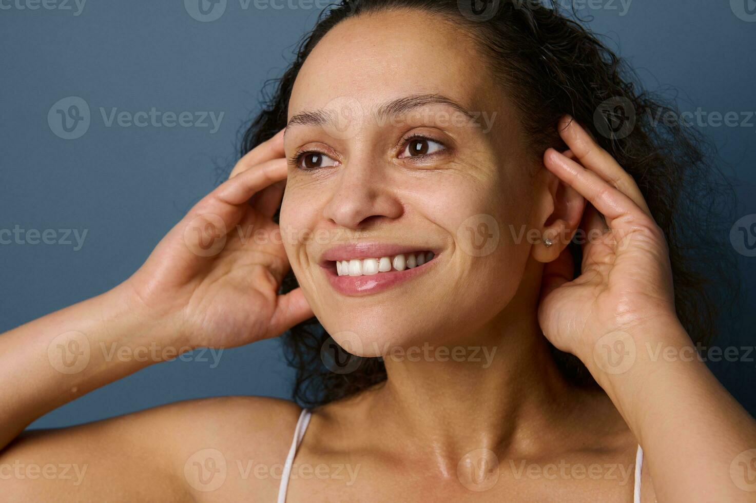 Close-up portrait of middle aged woman with no make-up and wet skin smiles toothy smile while washing her face, taking care of her beauty and skin. Freshness, purity, cleanse, removing make-up concept photo