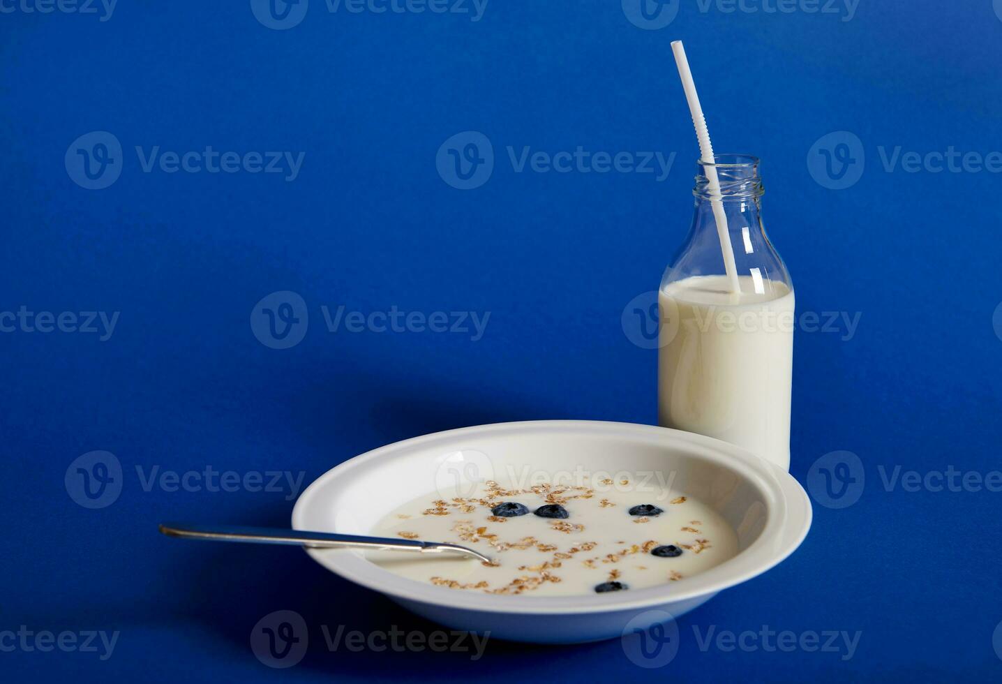 Closeup composition of fresh milk and a plate of muesli with berries, isolated on blue background photo