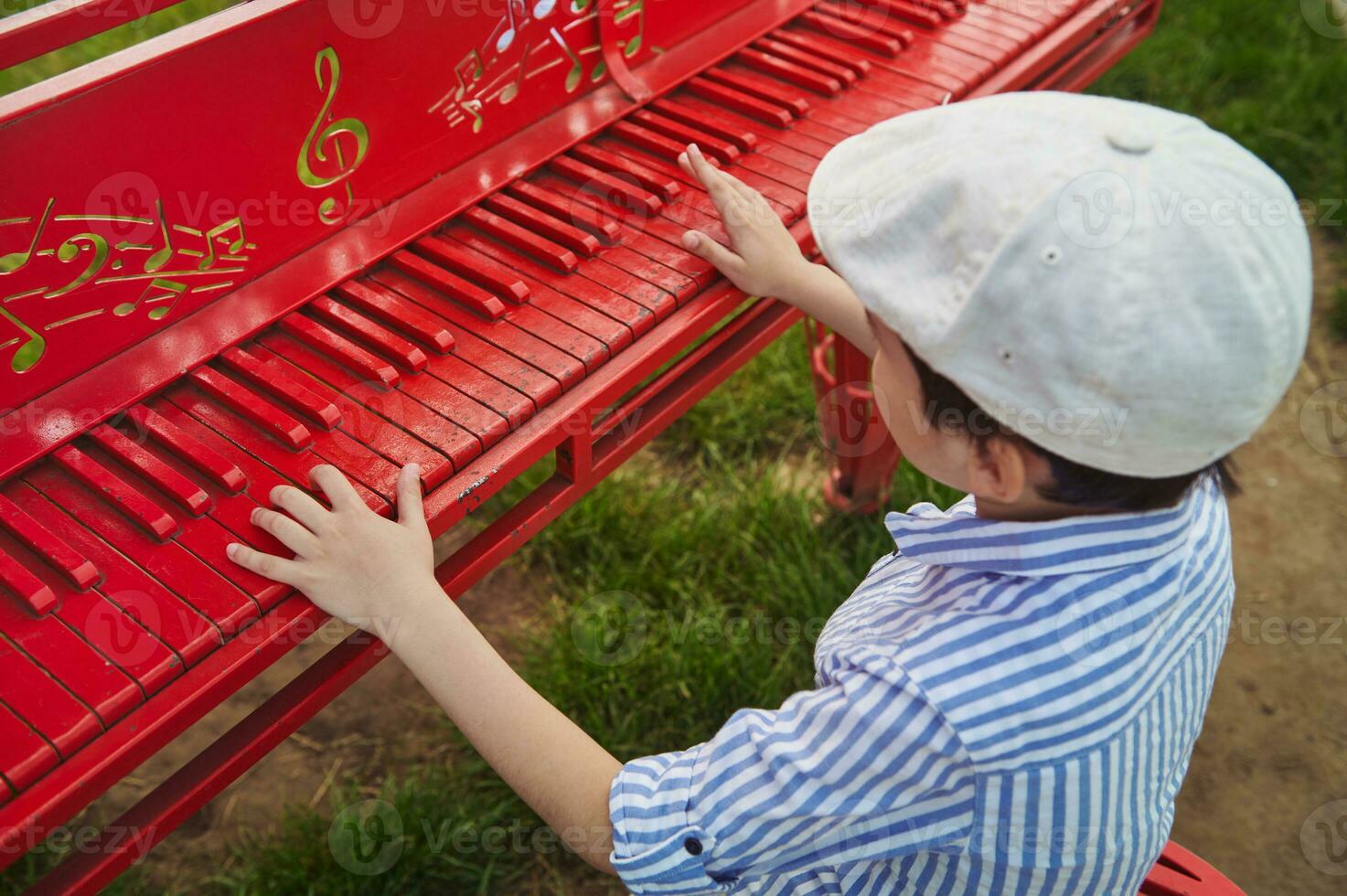 Boy in a beret plays the red piano outdoors on a beautiful sunny summer day photo