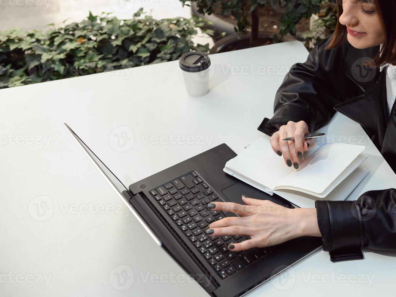 Overhead view of concentrated woman, business person, journalist, freelancer, copywriter, writing texts on notepad, typing on keyboard of a laptop computer. Online remote work and freelance concept photo