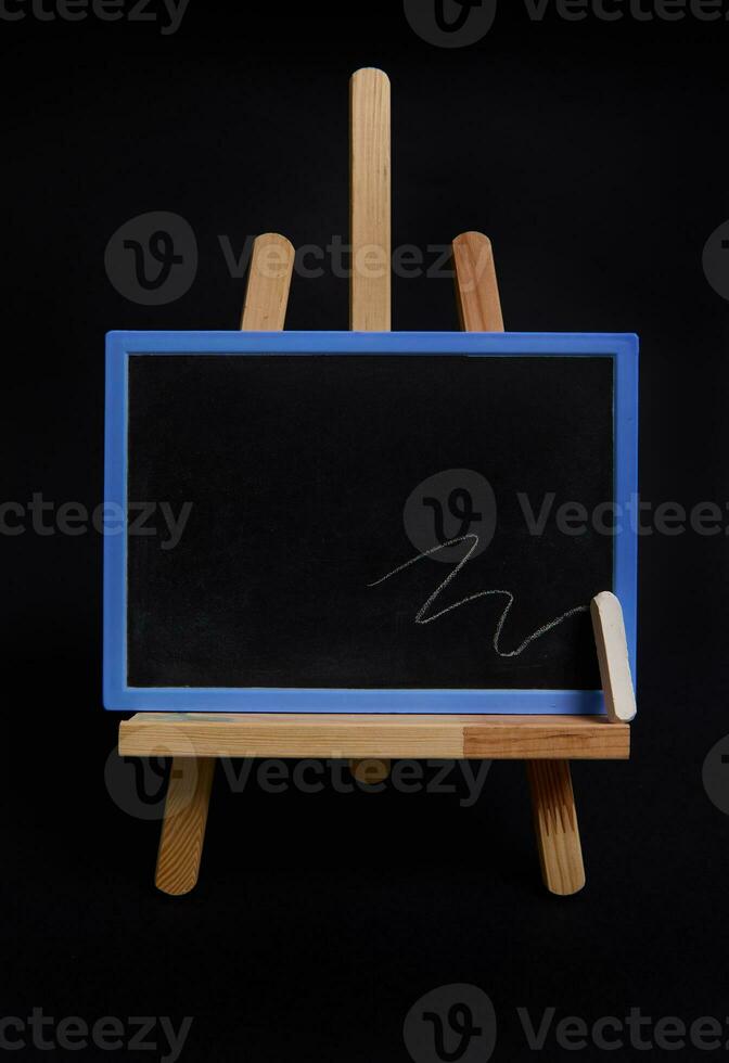 Close-up studio shot of a wooden table easel with a chalk and blackboard with empty blank space for text, isolated on black background photo