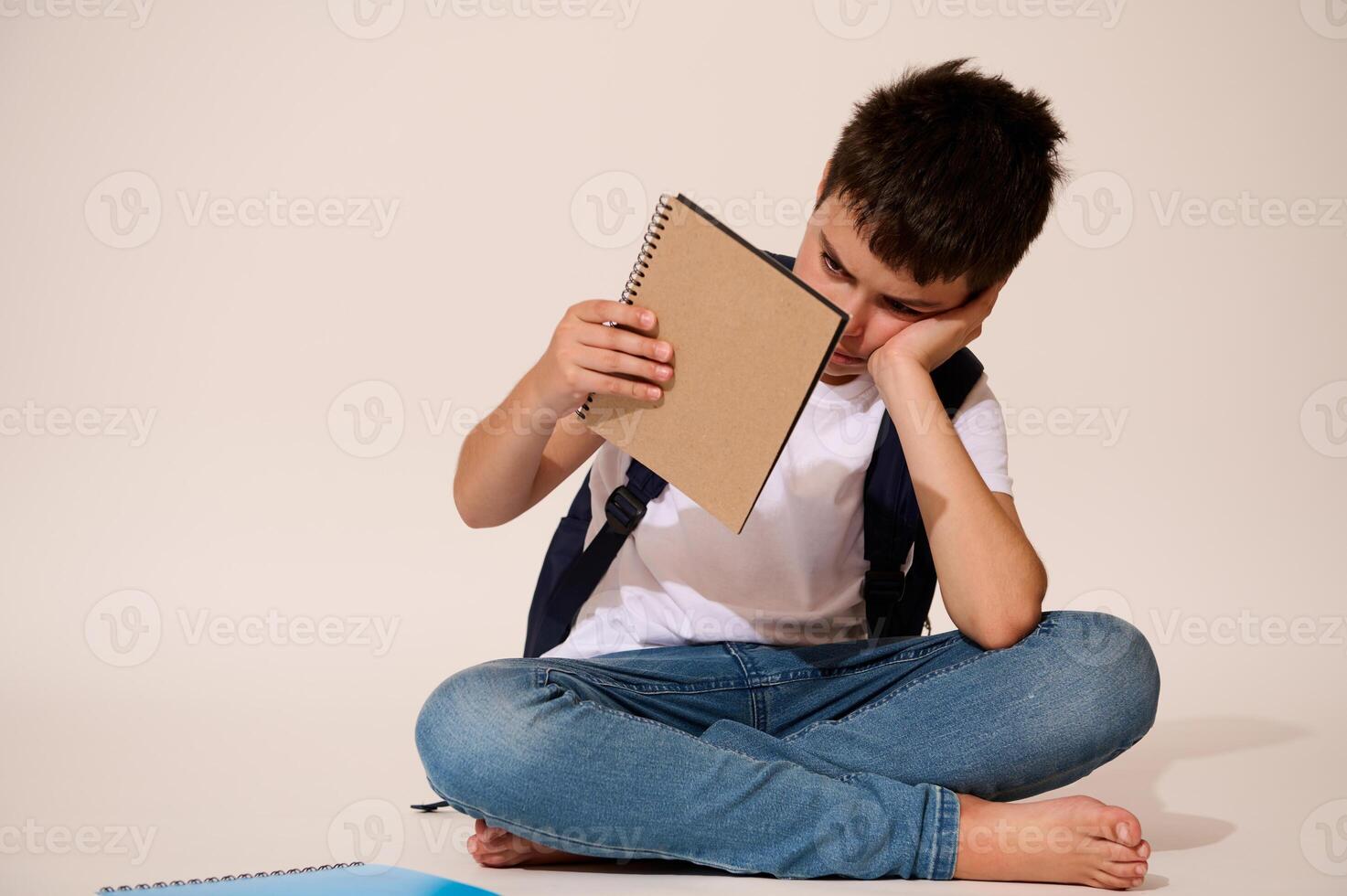 Studio shot of a bored upset demotivated schoolboy holding a copybook with free ad spacec, isolated on white background photo
