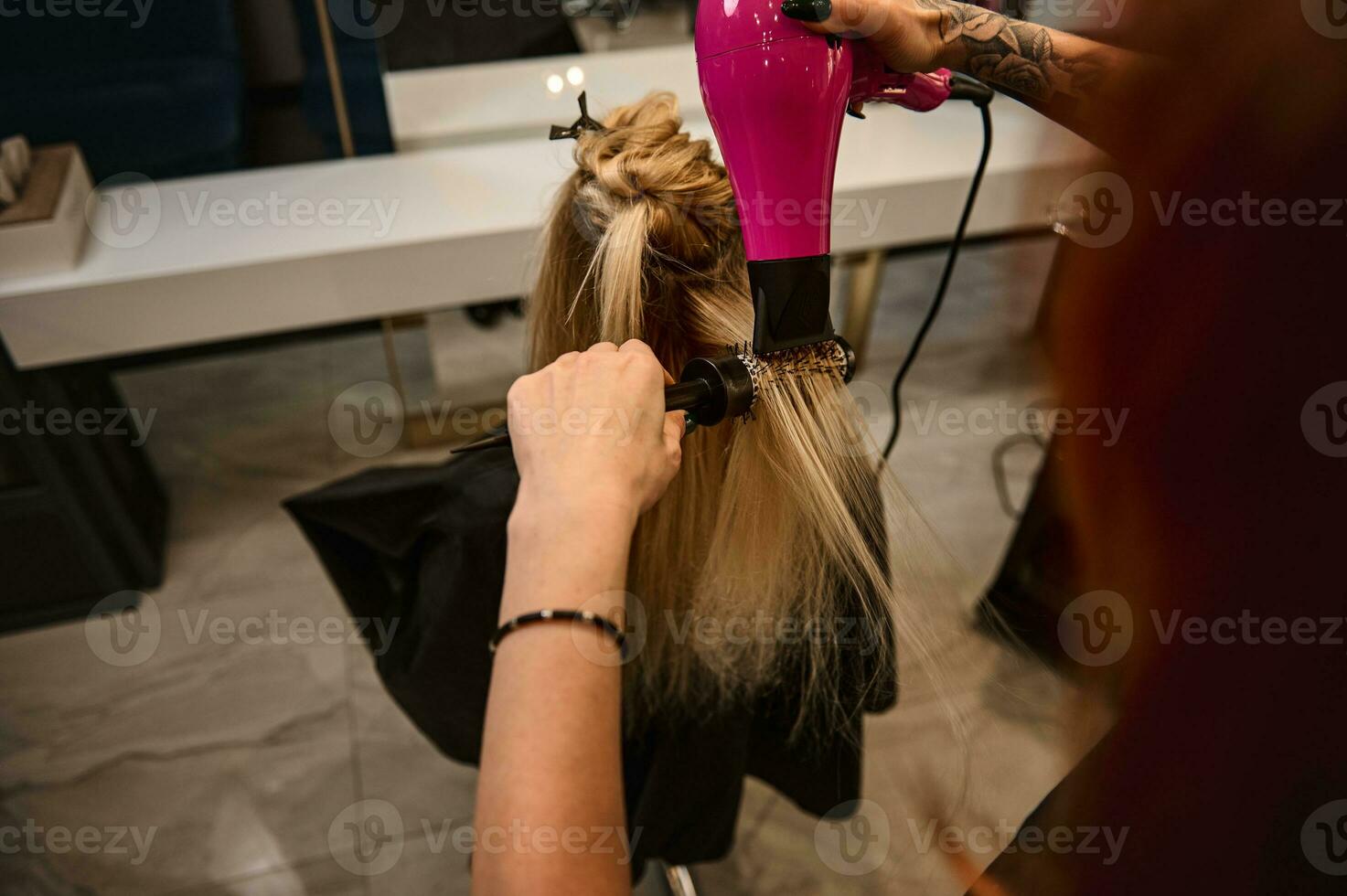 Close-up. Overhead view of redhead female hairdresser combing and drying client hair in beauty parlor, performing stylish hair style. Fashion, small business and beauty industry concept photo