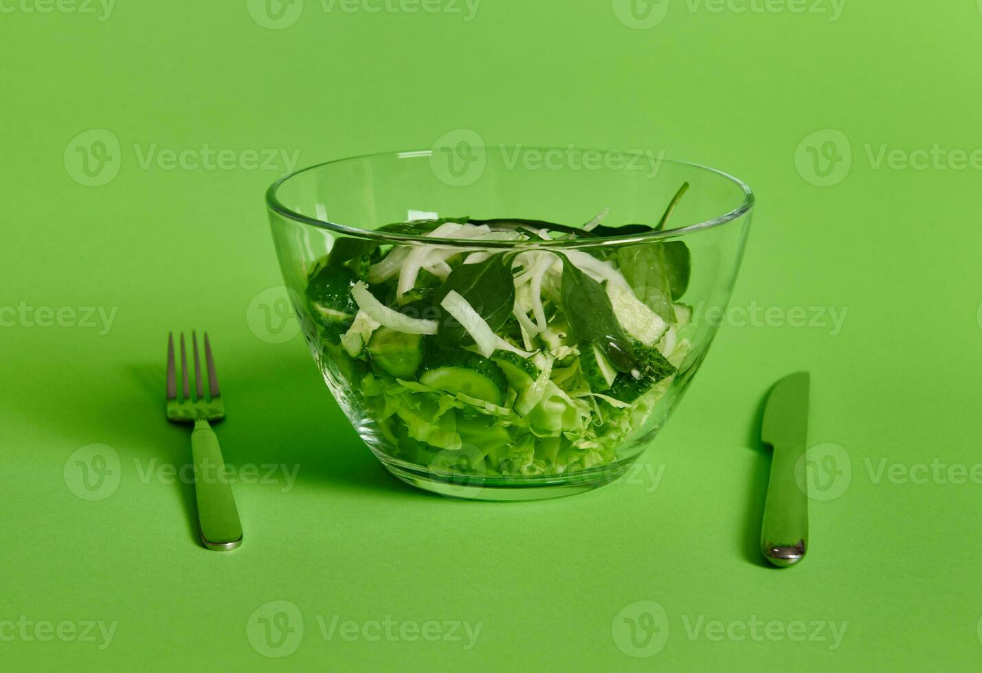 Fork and knife near a plate of green salad on green background with copy space photo