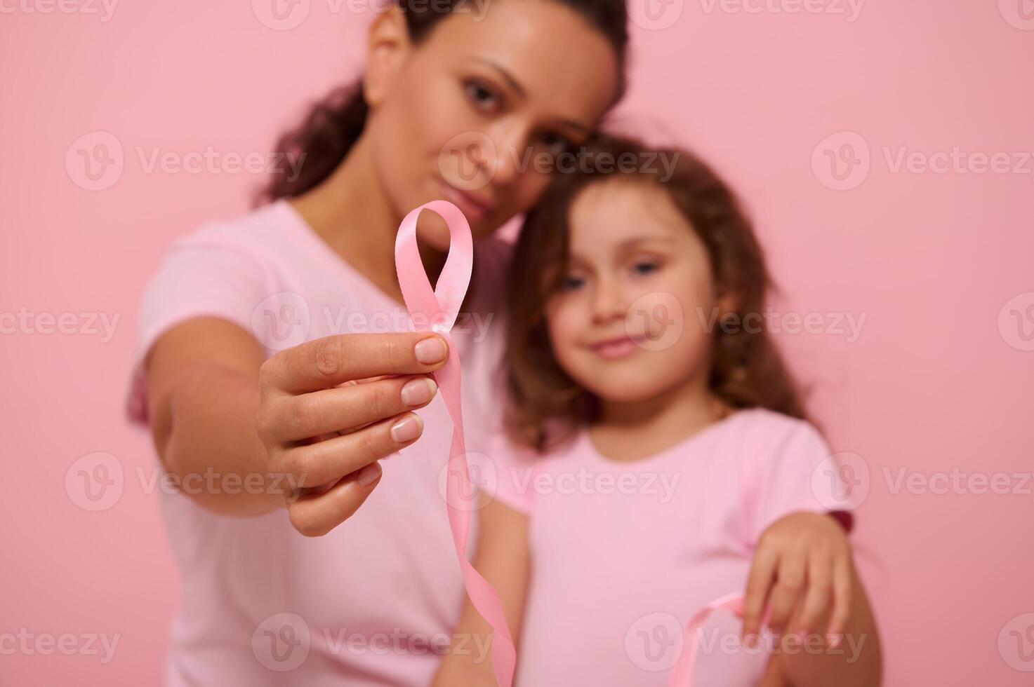 Focus on a long pink satin ribbon with one endless end in the hands of blurred two generations of pretty women, mom and daughter, expressing support and solidarity for cancer patients and survivors photo