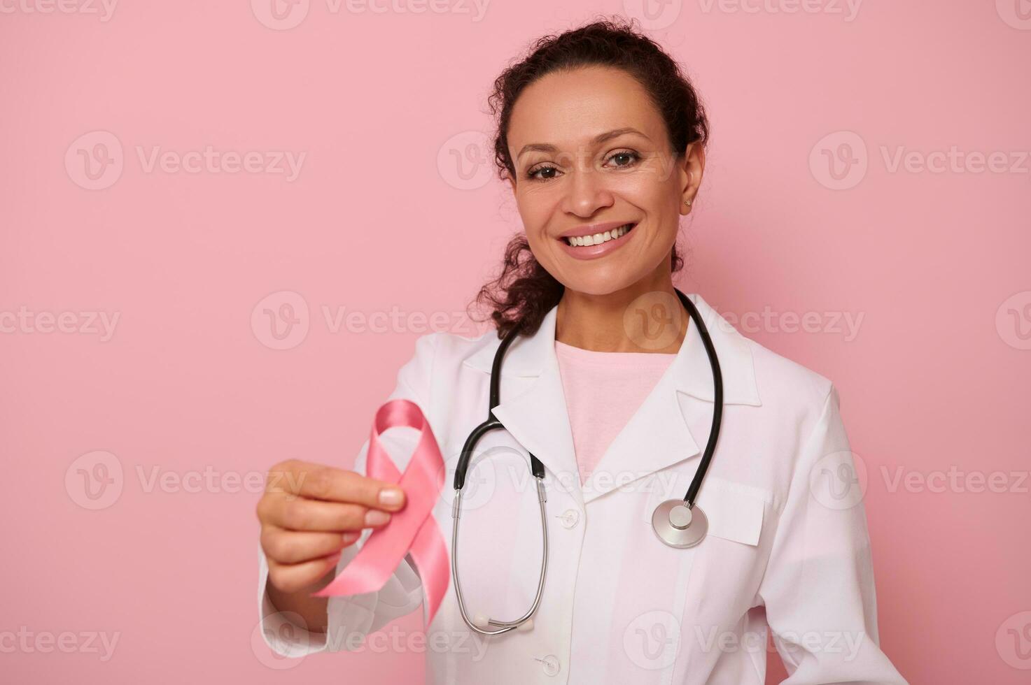 Gorgeous African American female doctor with beautiful toothy smile showing a Pink satin Ribbon, isolated on colored background with copy space. World Day of fight Breast Cancer, 1 st October concept photo