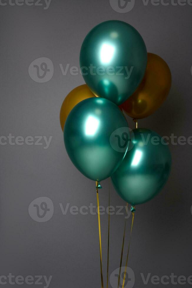 Close-up studio shot for advertising of colorful golden and metallic green inflated air balloons, isolated over gray background with copy space. Birthday, Anniversary, events and Christmas concept photo