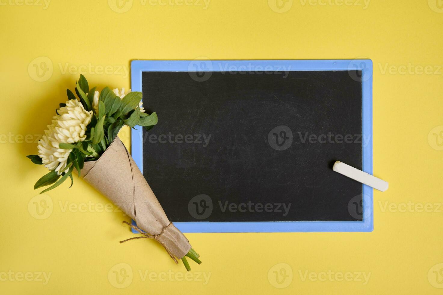 plano laico composición de delicado hermosa elegante ramo de flores de ásteres flores en arte envase papel atado con un cuerda en un blanco vacío pizarra con espacio para texto aislado en amarillo antecedentes foto