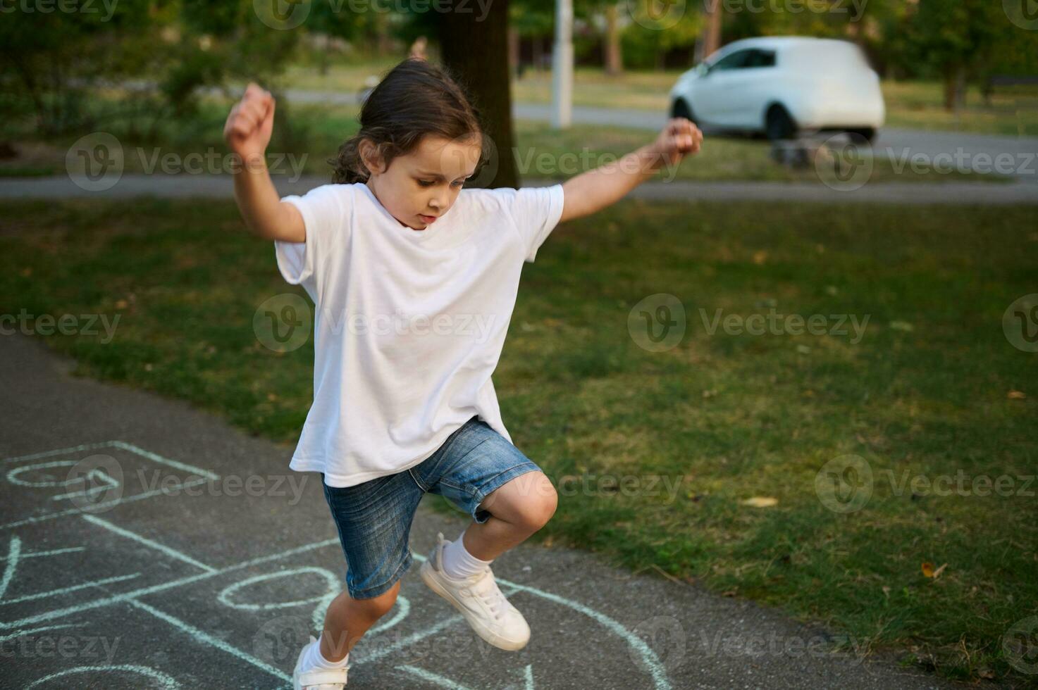 Closeup of little Caucasian girl playing hopscotch on asphalt. Child playing hopscotch game on playground outdoors on a sunny day. Street children's games in classics. photo