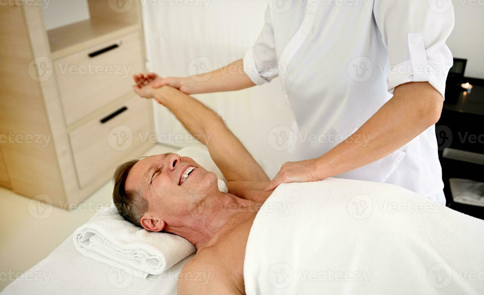 Unrecognizable female massage therapist performing body massage to a handsome mature man, client of luxury wellness spa center. Male body care, beauty treatment concept, copy space for advertisement photo