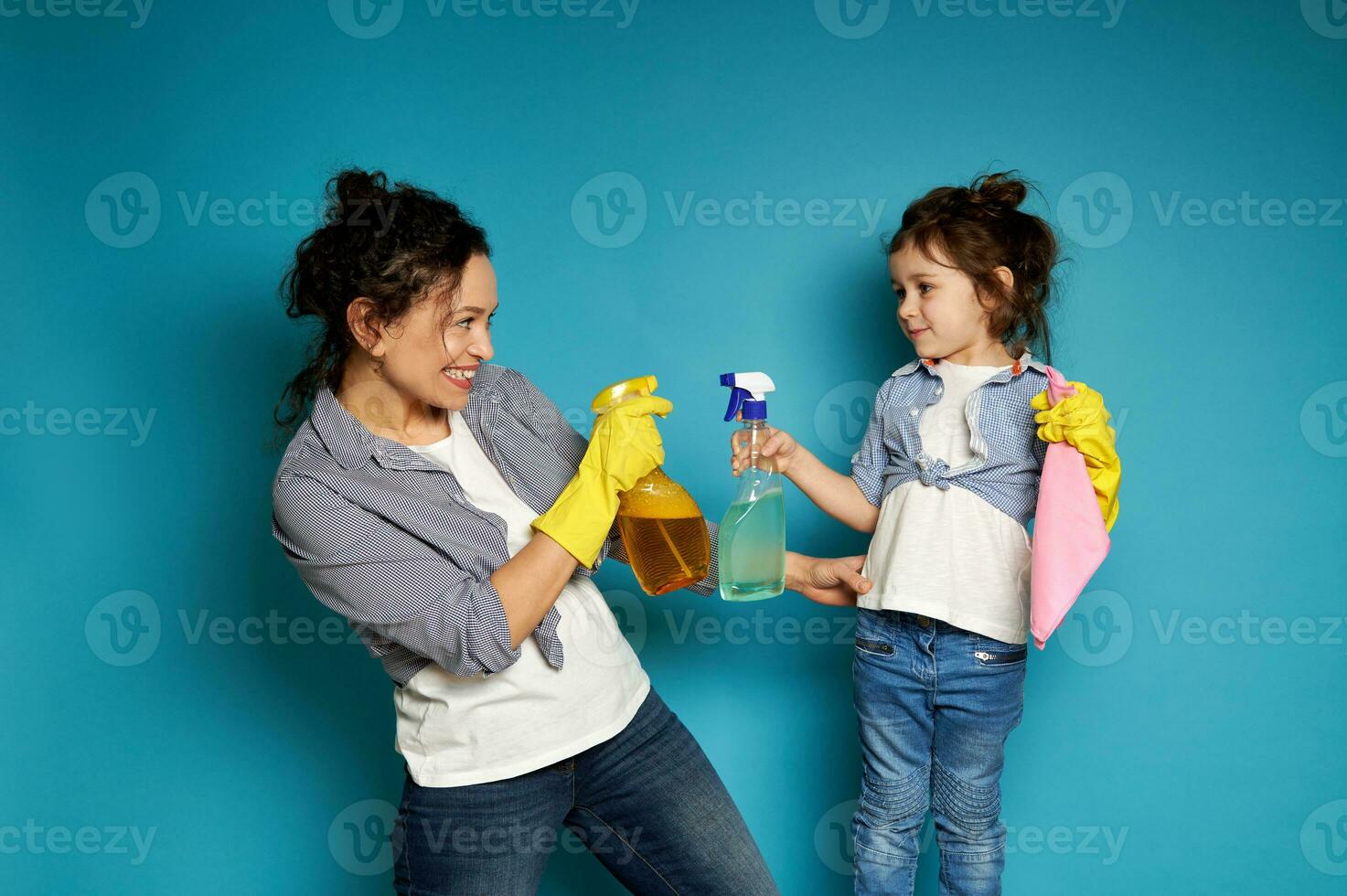 Cheerful mother and daughter hold a cleaning spray while playing with detergents. Household together. photo