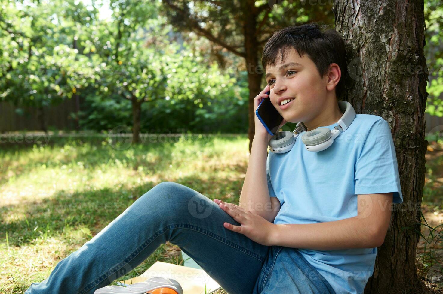 Authentic portrait handsome teenage schoolboy talking on smart mobile phone while chilling out in the park after school. photo