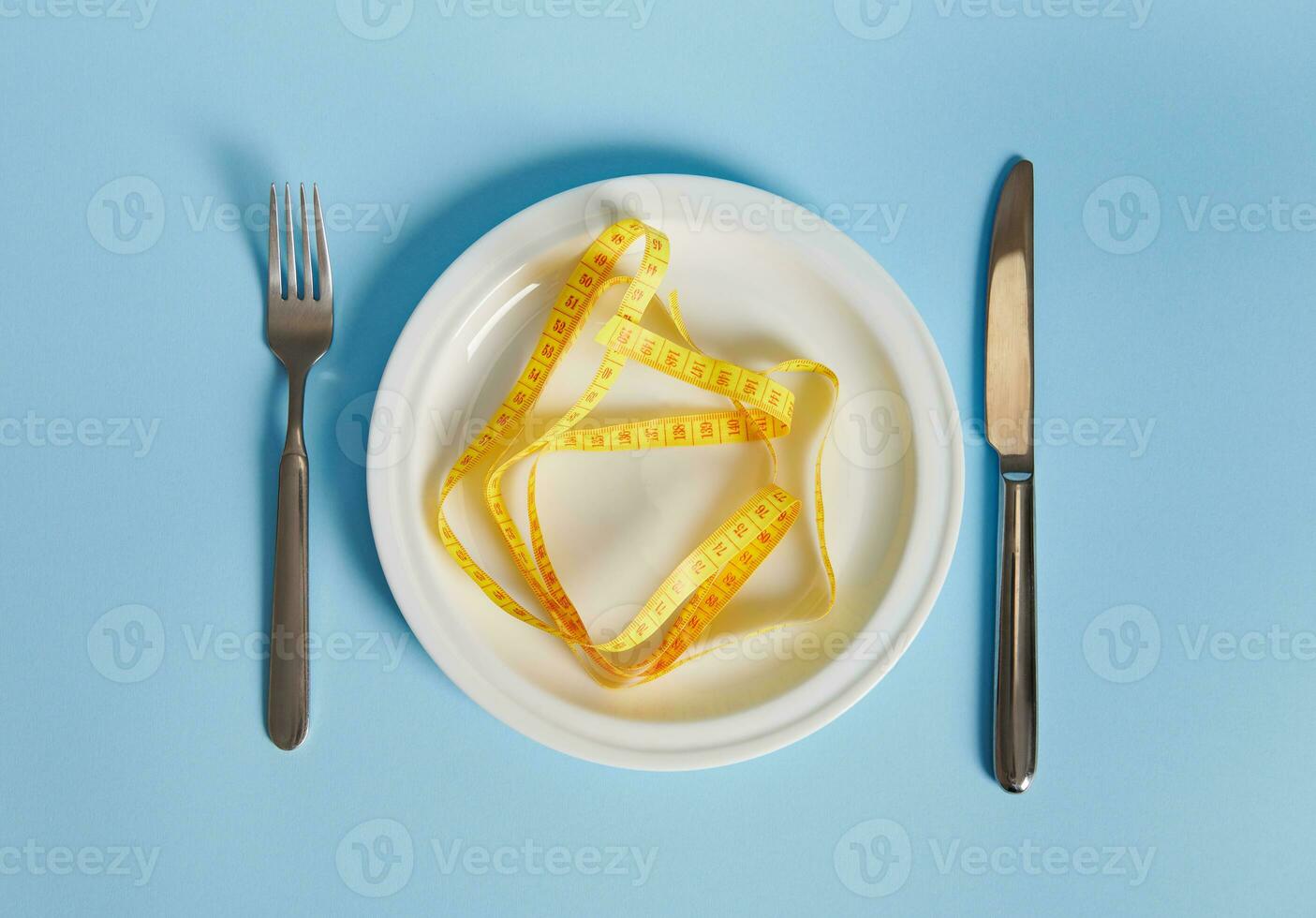 Knife, fork and measuring tape on an empty plate. Diet concept on blue background with copy space photo