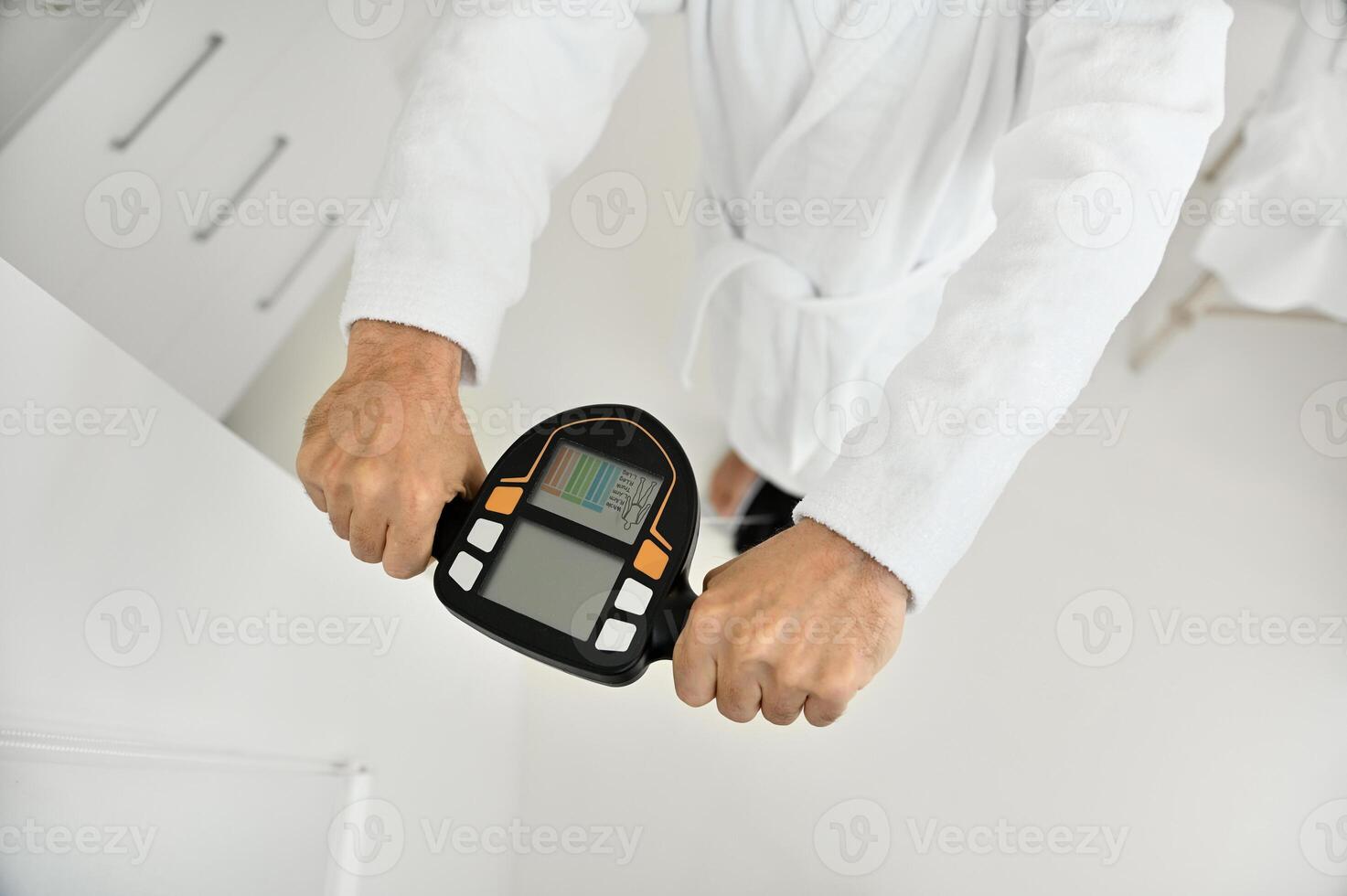 Top view of male hands holding the handle of a smart scale. Close-up of a mature man's hand in a white terry bathrobe weighing on a medically smart scale to determine the biological age and vitality photo