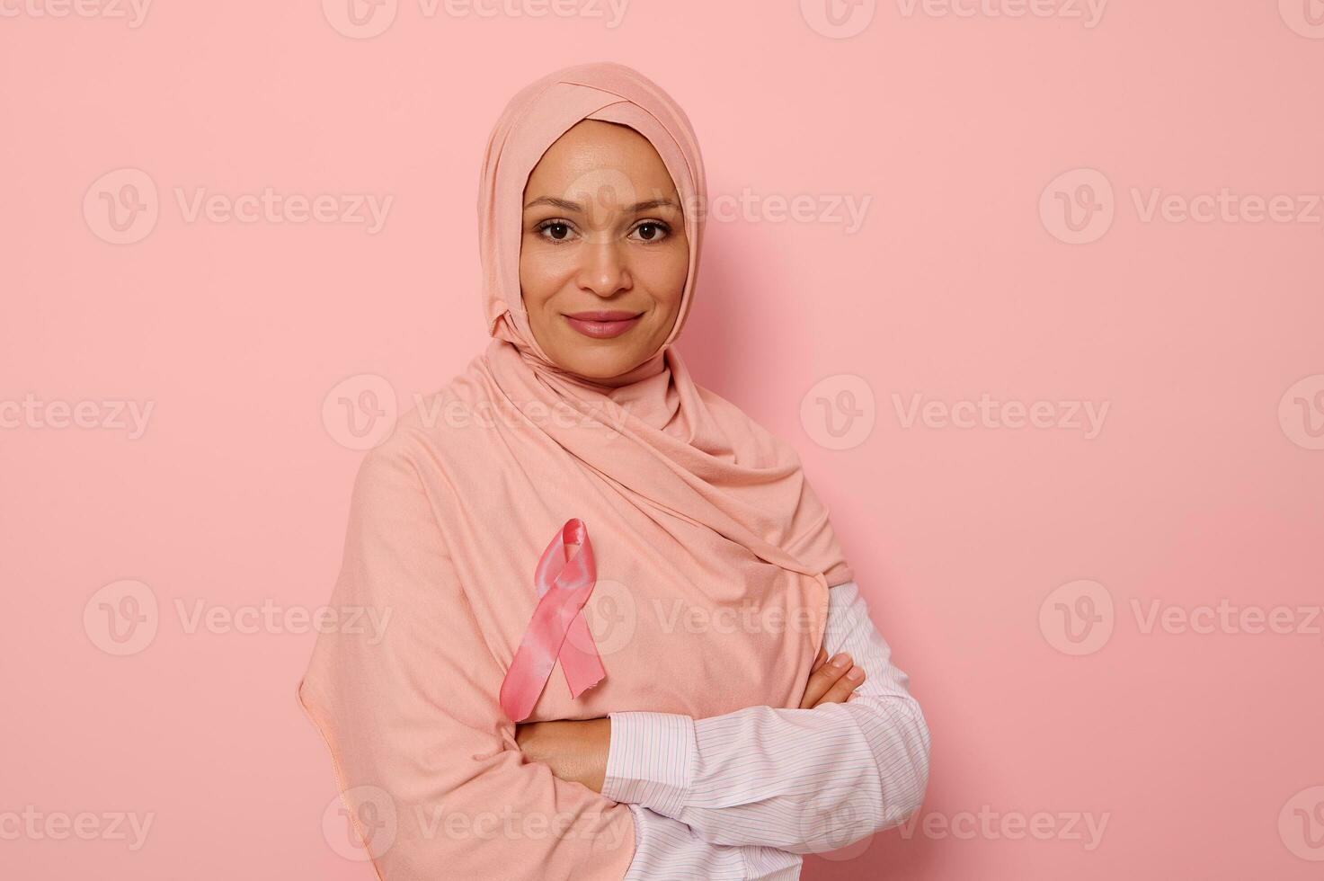 confidente retrato de un simpático árabe musulmán mujer vistiendo un hijab y rosado satín cinta demostración su apoyo para cáncer pacientes y sobrevivientes mundo pecho cáncer conciencia día. De las mujeres salud cuidado foto