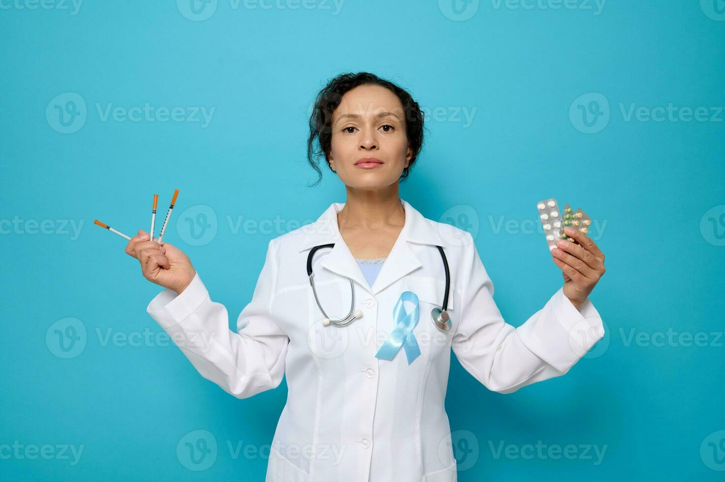 World diabetes day. 14 November. Female doctor in white medical gown wearing blue awareness ribbon holds insulin syringes, pharmaceutical tablets in blisters, isolated on blue background, copy space photo