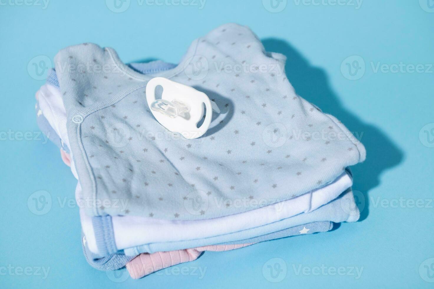 Still life with a baby comforter and clean baby clothes prepared for the birth of child, isolated over blue background photo