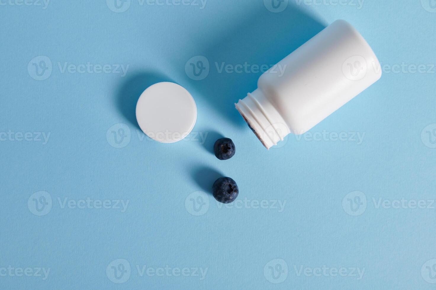 Flat lay composition of blueberries scattered from an opened white container on blue background photo