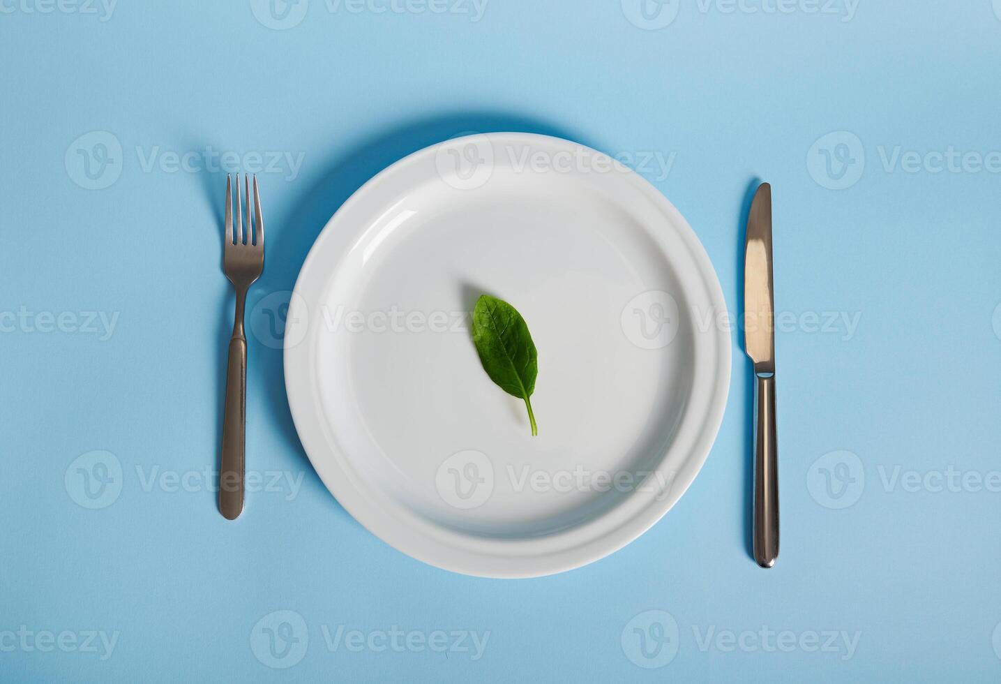 Flat lay composition with spinach leaf on a plate, fork and knife isolated on blue background. Healthy eating concept. photo