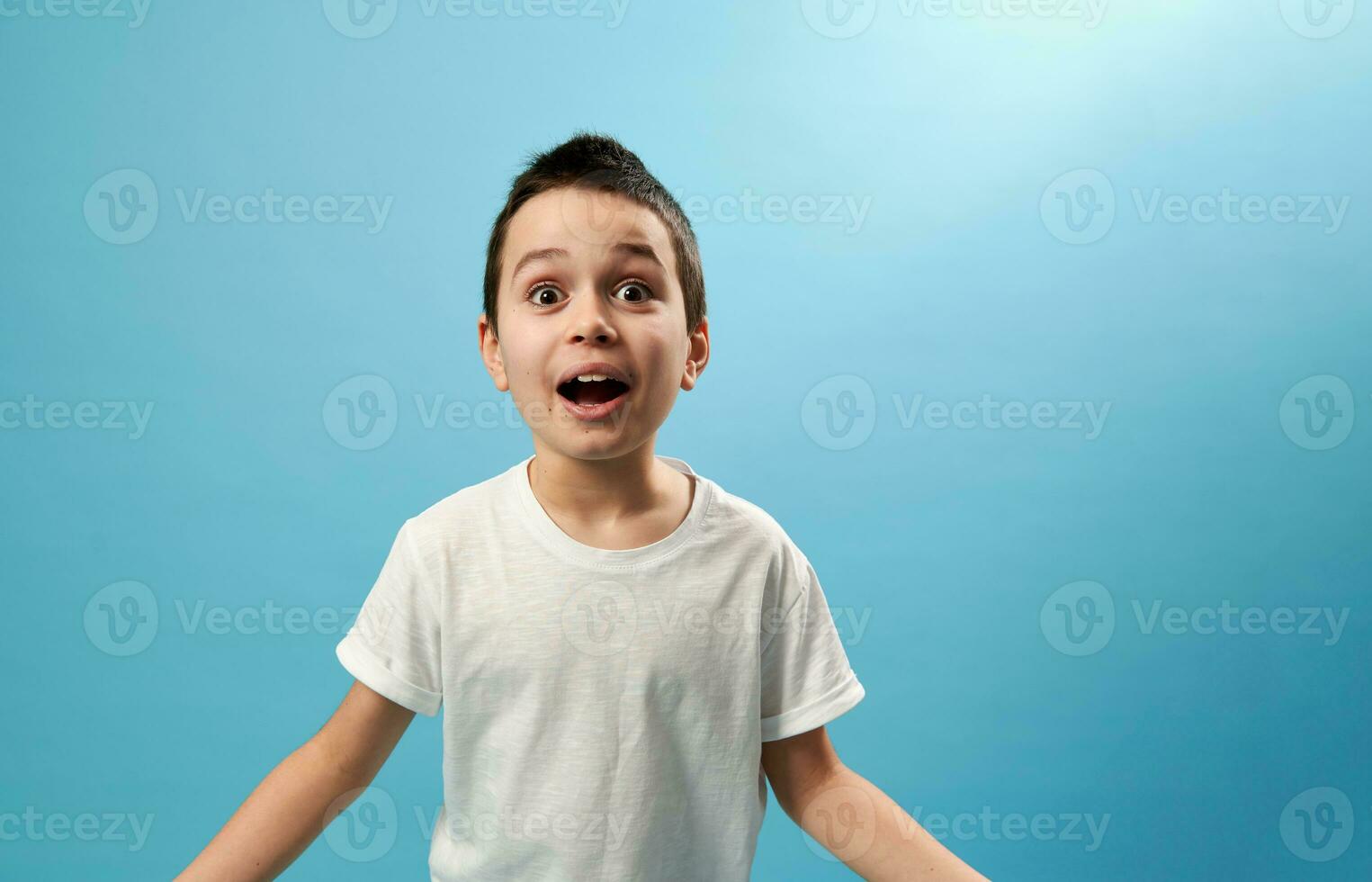 Shocked schoolboy expressing surprise on camera. Facial emotions on blue background photo