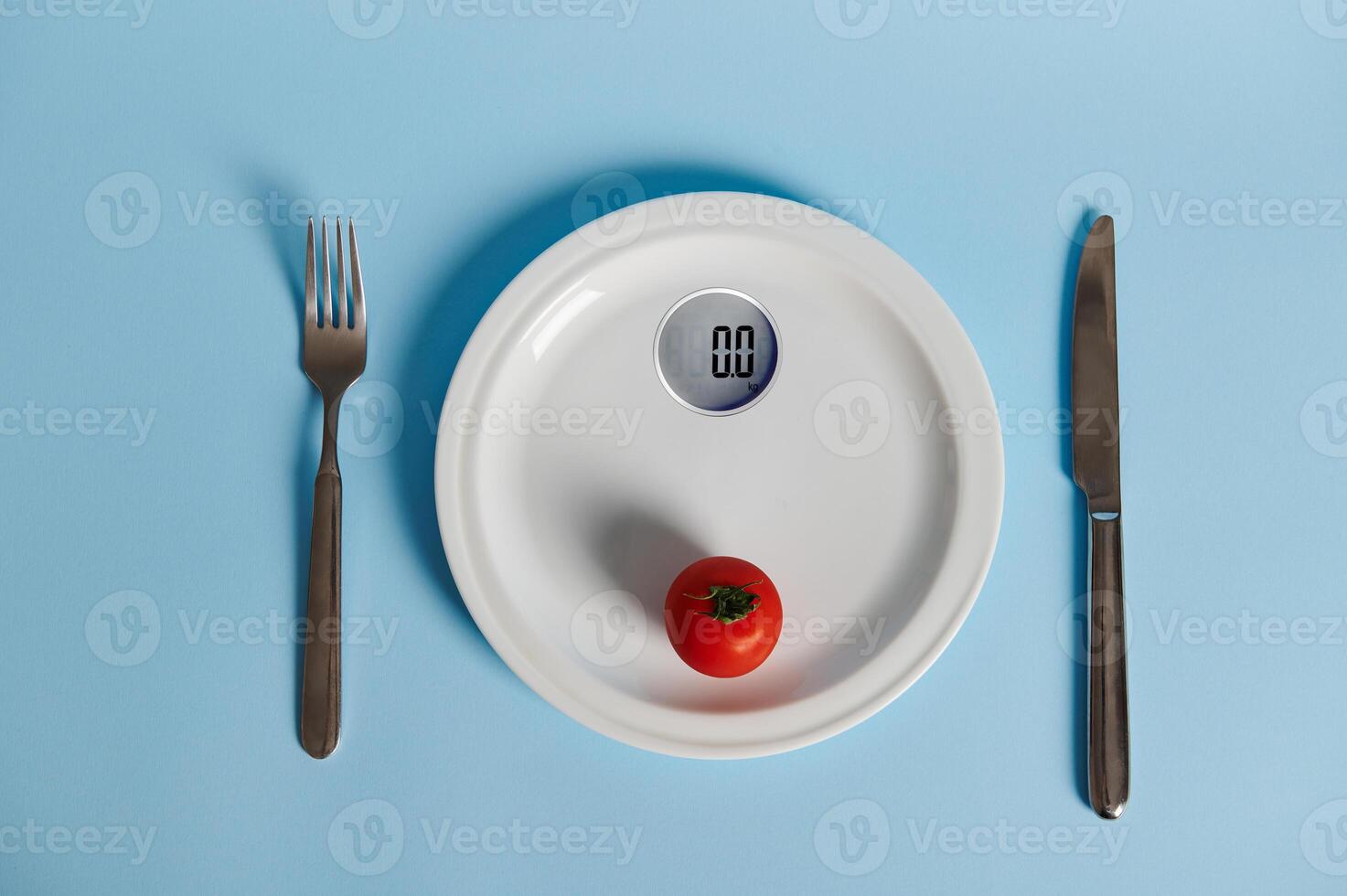 cuchillería y tomate en un plato en el formar de medición escamas, aislado en azul antecedentes con Copiar espacio foto