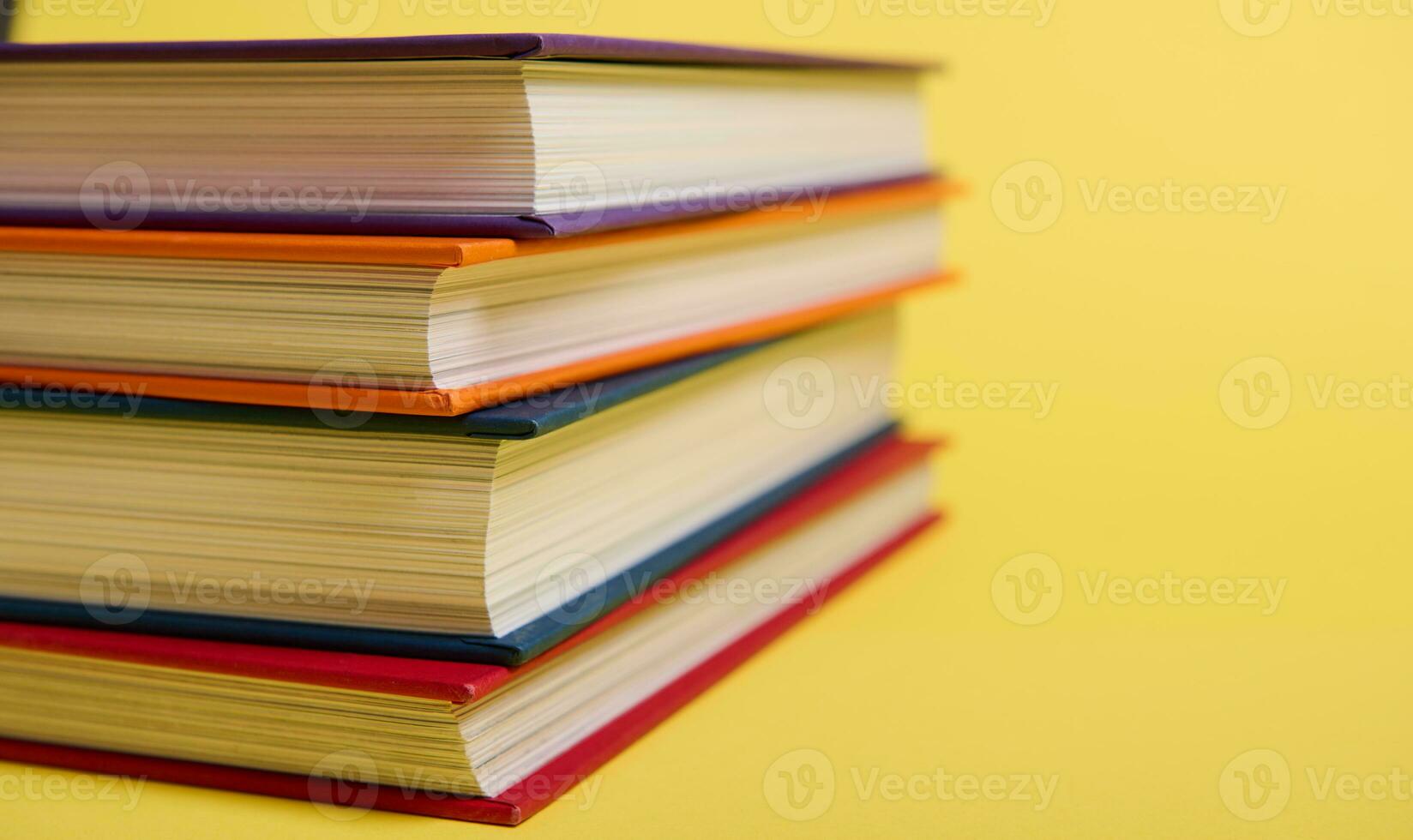 Close-up of stacked multicolored books on yellow surface background with copy space for text. Teacher's Day concept, Knowledge, literature ,reading, erudition photo