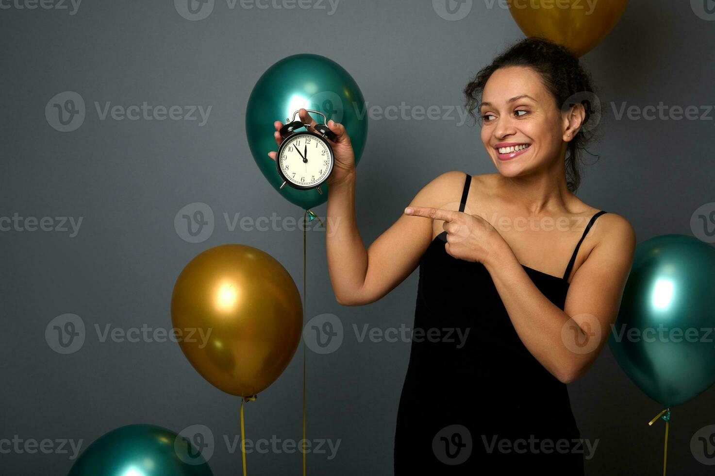 maravilloso mezclado carrera mujer vistiendo un noche vestido, puntos en un alarma reloj aislado terminado gris antecedentes con dorado y verde metálico aire globos Navidad, nuevo año, cumpleaños fiesta, aniversario foto