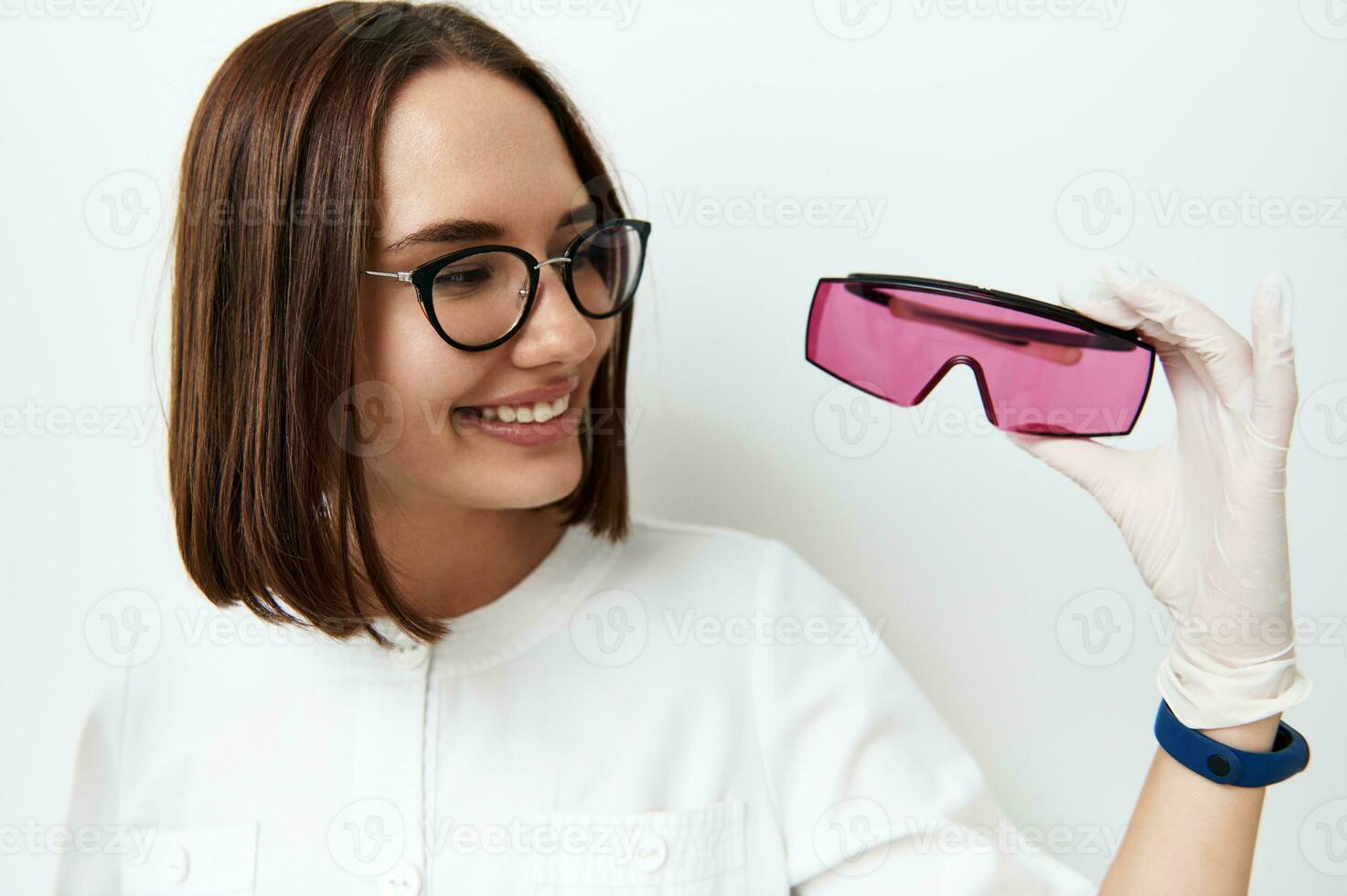 Beautiful smiling young doctor looking at protective UV googles in her hand photo