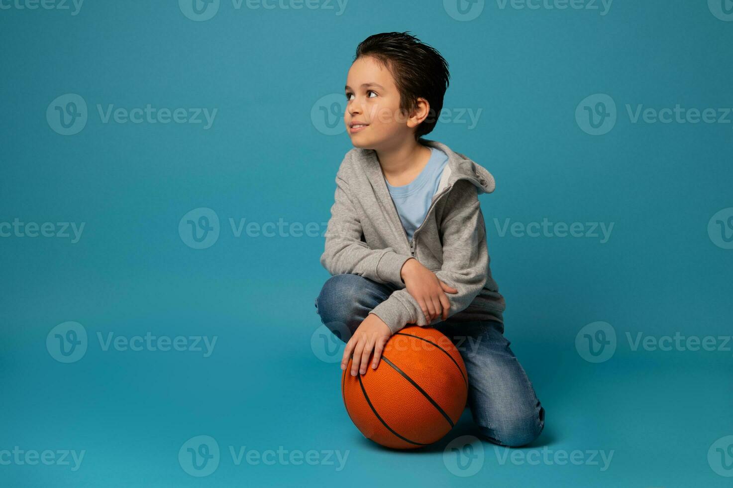 Beautiful sporty teenage boy posing with a ball for playing basketball over blue background photo