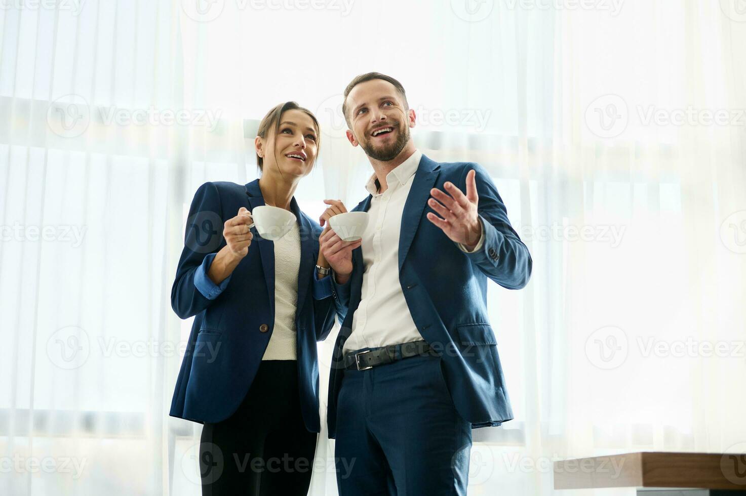 dos hermoso negocio socios en Armada casual trajes participación taza de café y negociando gesticulando y mirando aparte en uno dirección. exitoso asociaciones concepto, trabajo en equipo, colaboración foto