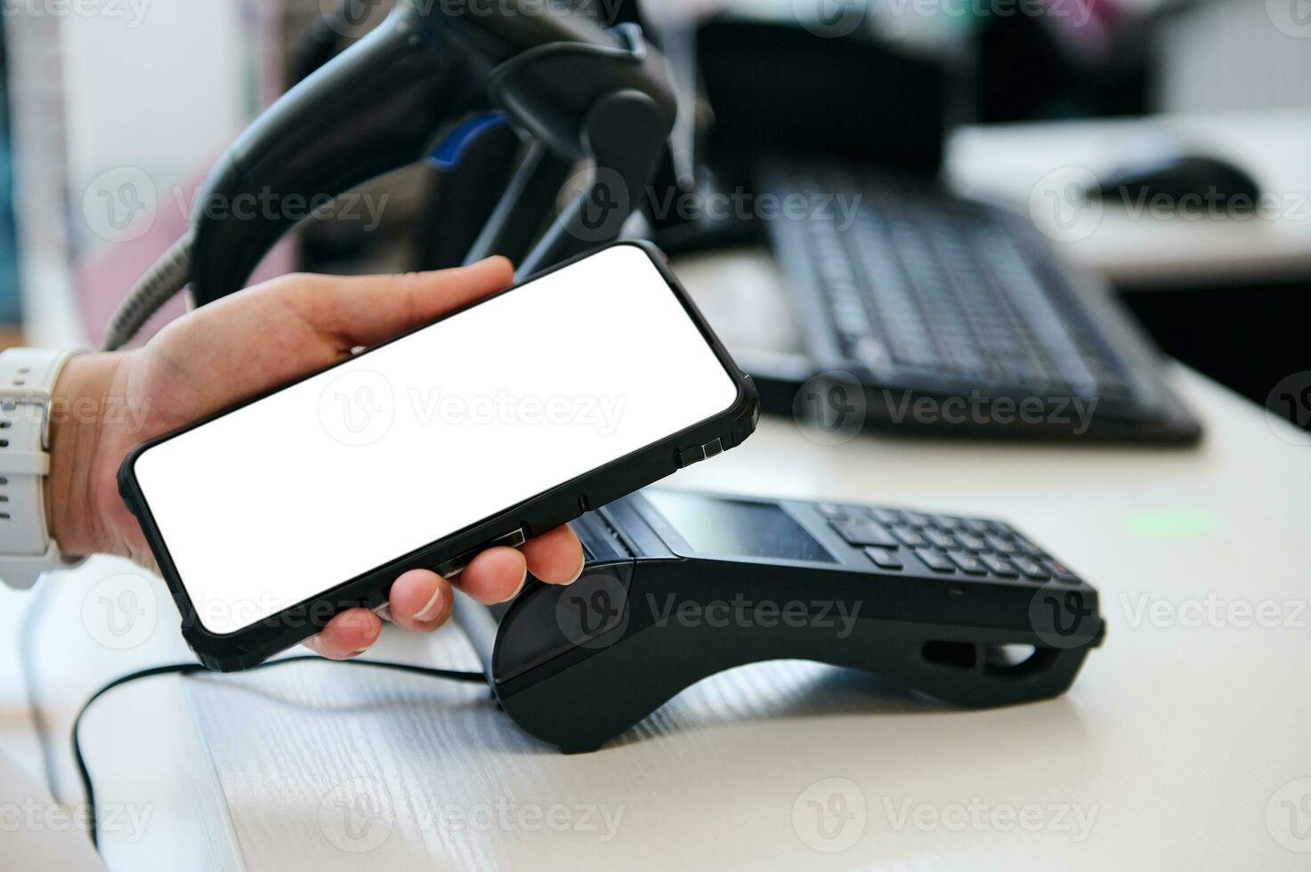 Close-up hand of customer holding smartphone with white mockup digital screen over a credit card reader, paying via NFC photo