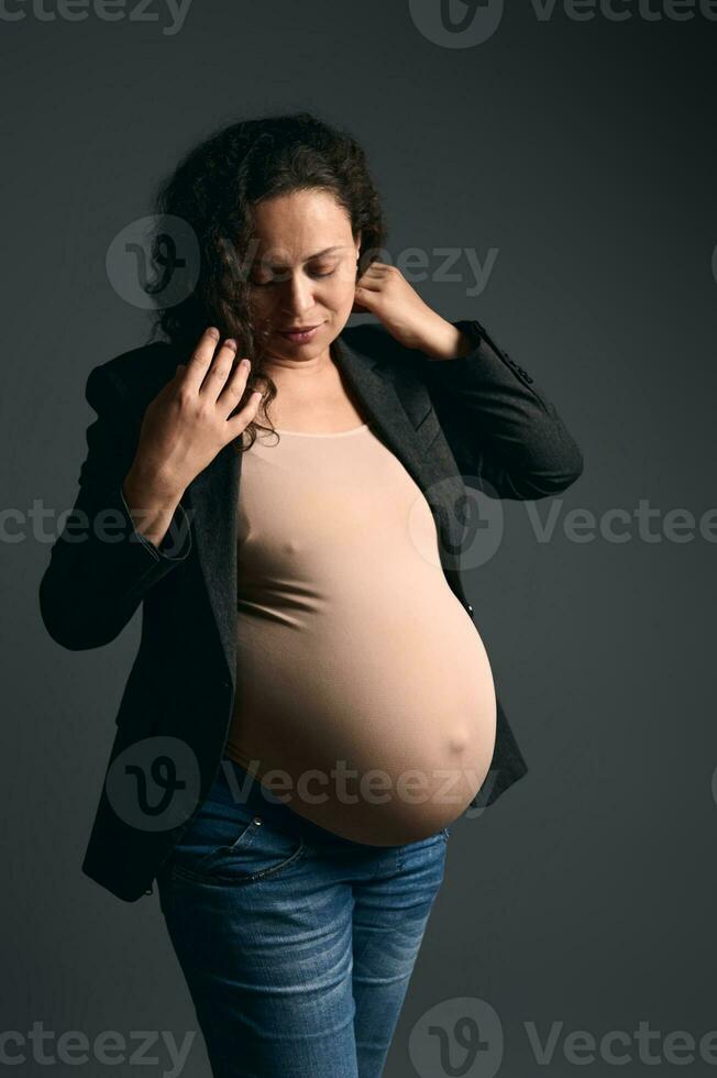 auténtico adulto embarazada posando en contra un Moda gris estudio antecedentes. hermosa el embarazo. maternidad estilo de vida foto