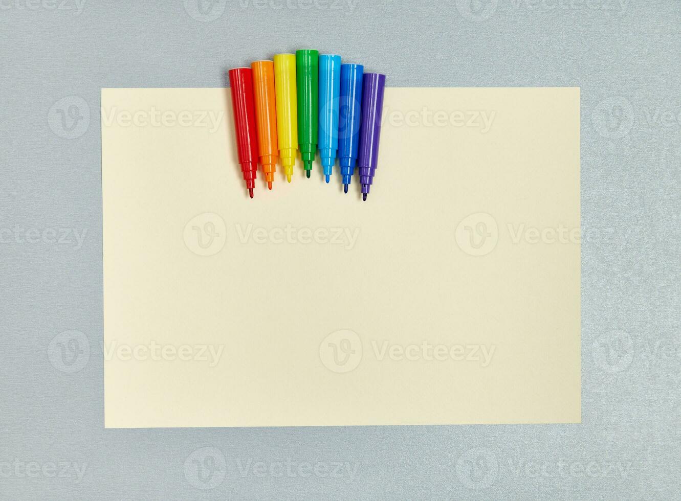 Rainbow-colored markers on yellow drawing paper. Flat lay. Top view photo